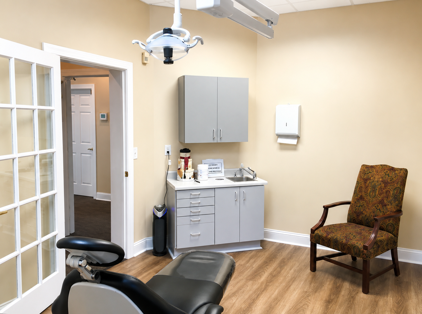 Dental exam room with chair, overhead light, cabinets, sink, and a patterned waiting chair