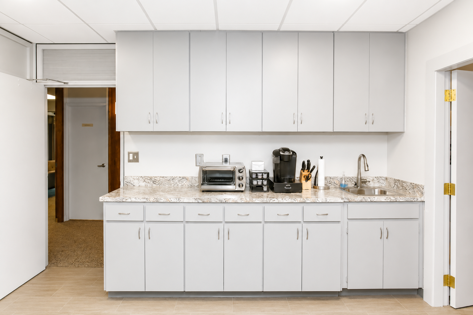 Bright white kitchen counter with cabinets, sink, and coffee maker under overhead storage cabinets