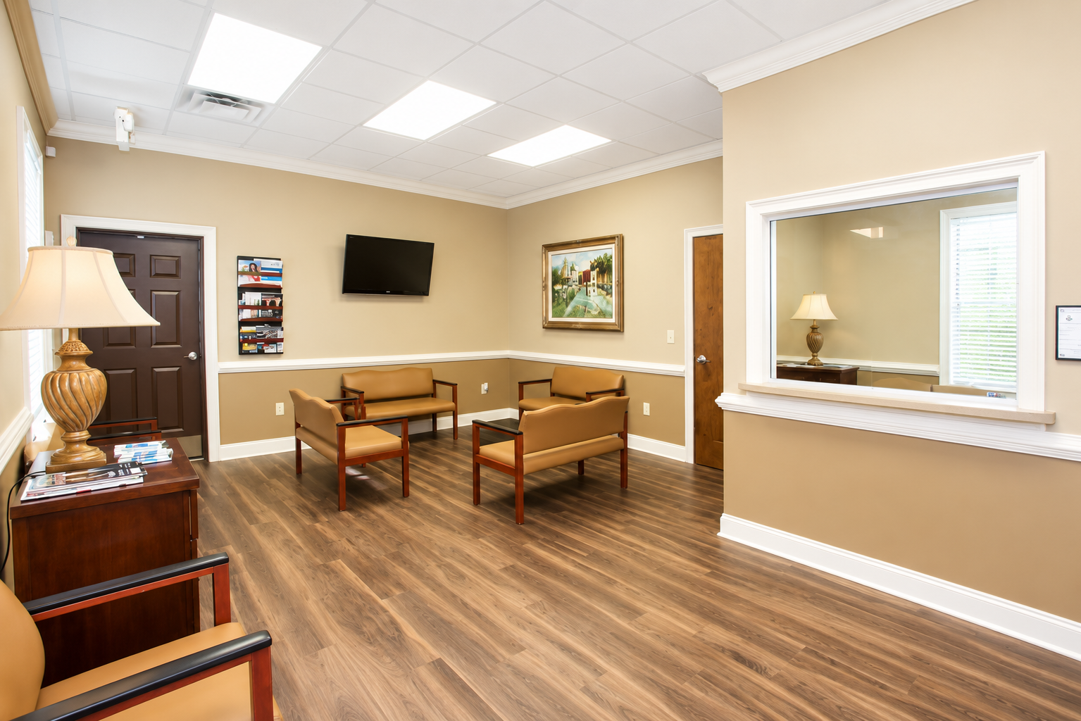 Waiting room with beige walls, wood floors, chairs, wall art, and a TV
