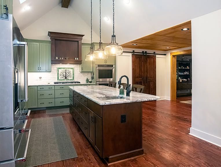 Modern kitchen with dark wood island, marble countertops, green cabinets, and warm pendant lighting