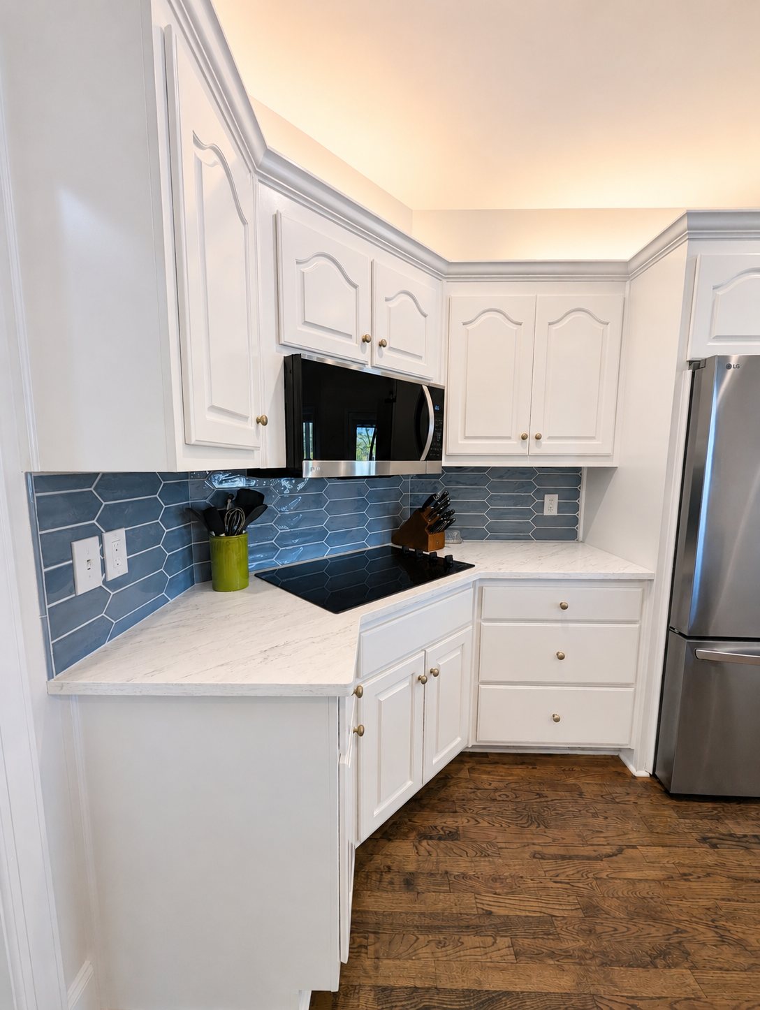 Bright white kitchen with blue tile backsplash, stainless fridge, and wood floor