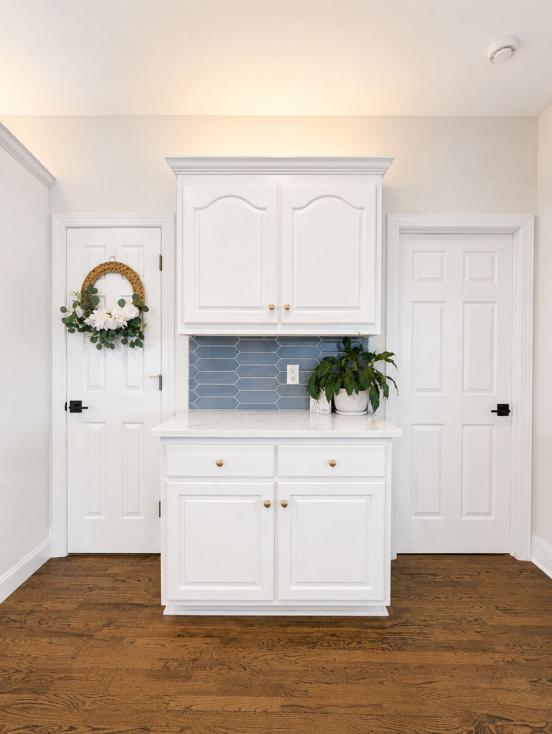Bright white mudroom with cabinets, blue tile backsplash, and two doors over a brown floor.