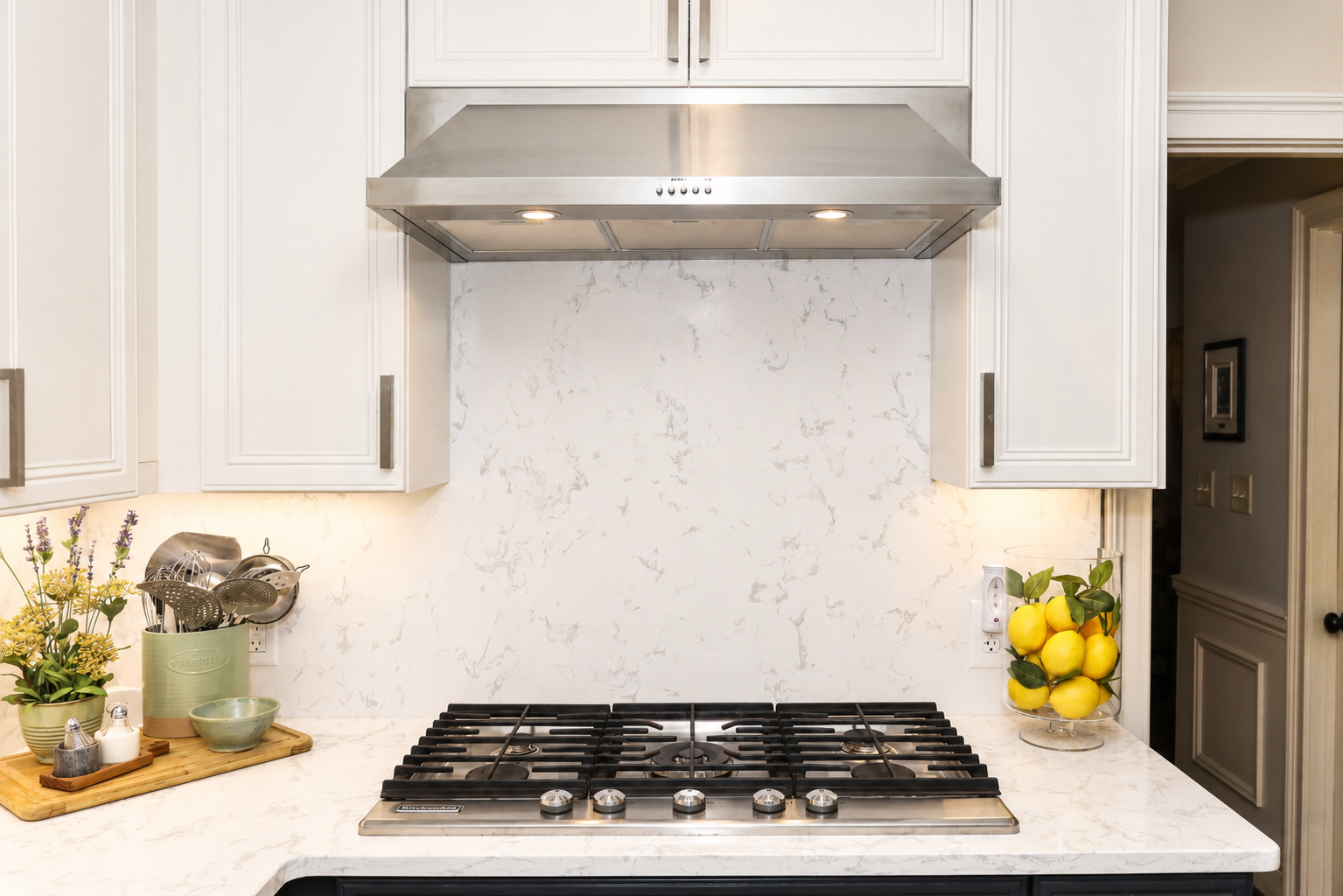 Modern white kitchen with stainless gas stove, range hood, and lemon decor on the counter