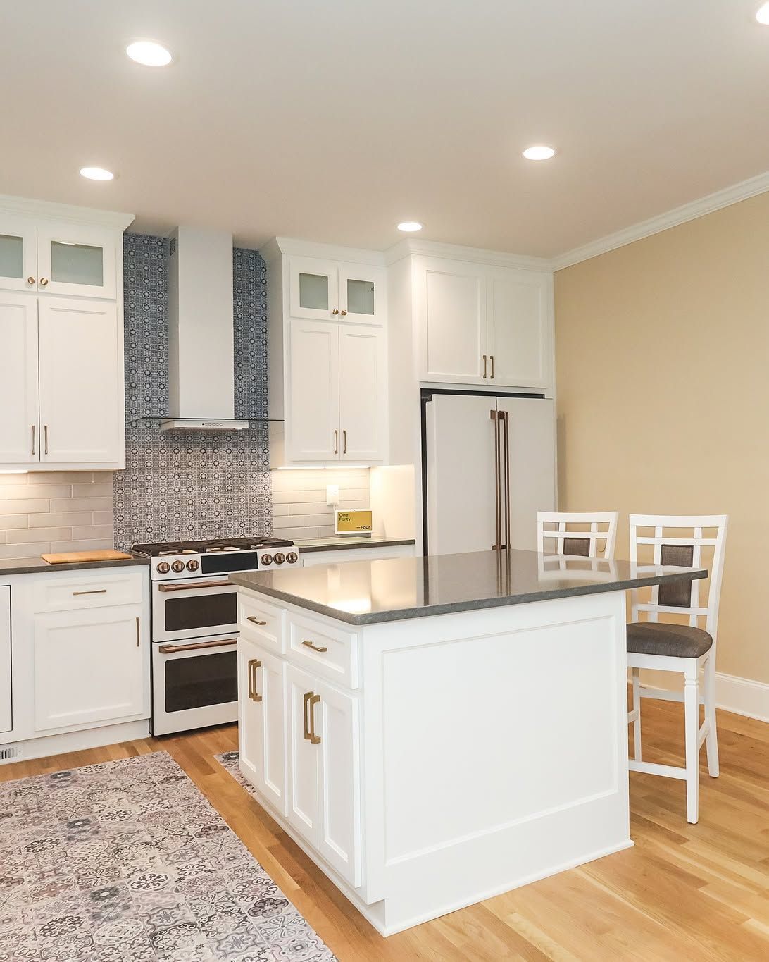 Bright white kitchen with island, stainless fridge, tiled backsplash, and hardwood floor