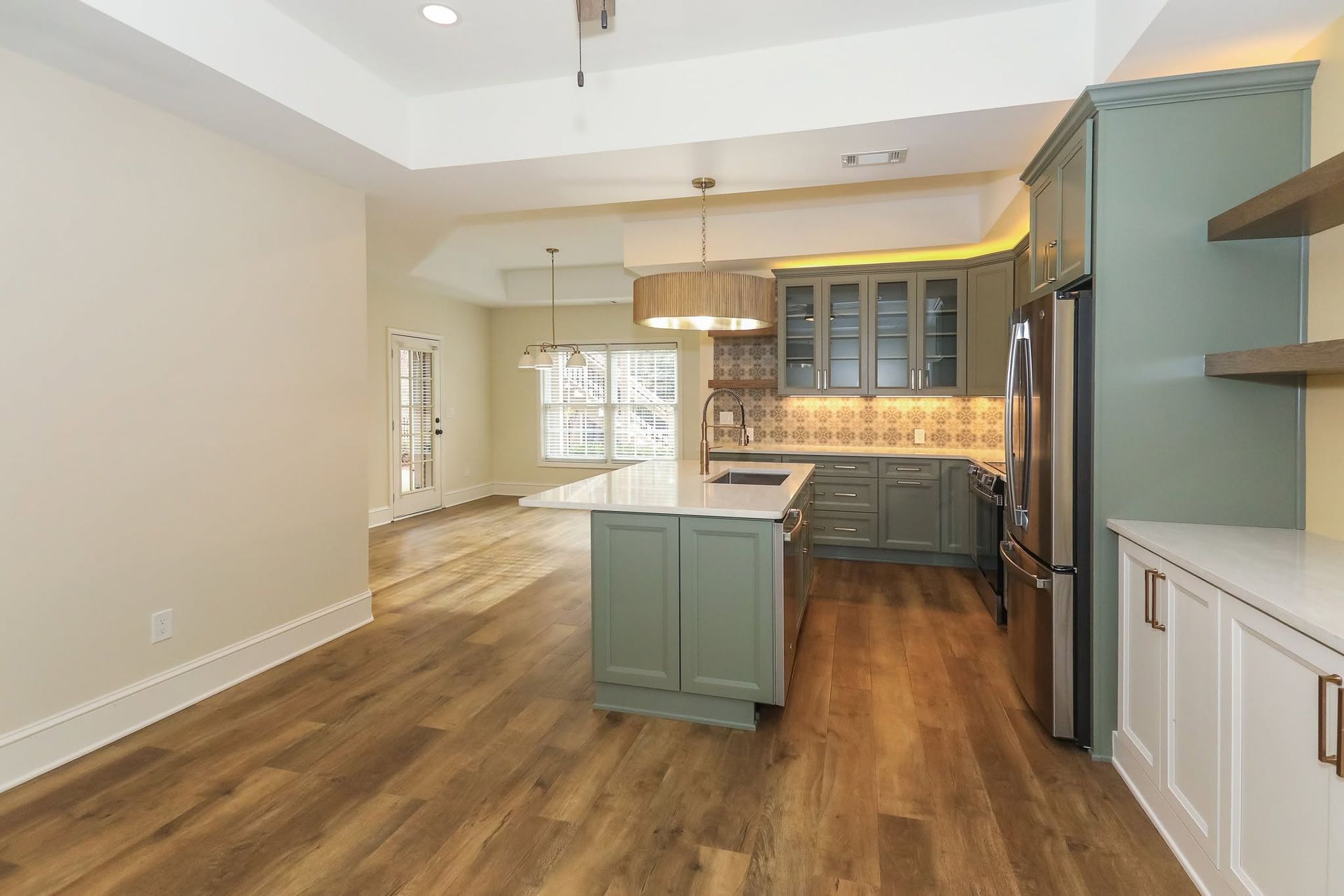Open-concept kitchen with teal cabinets, wood floors, island, and stainless steel refrigerator.