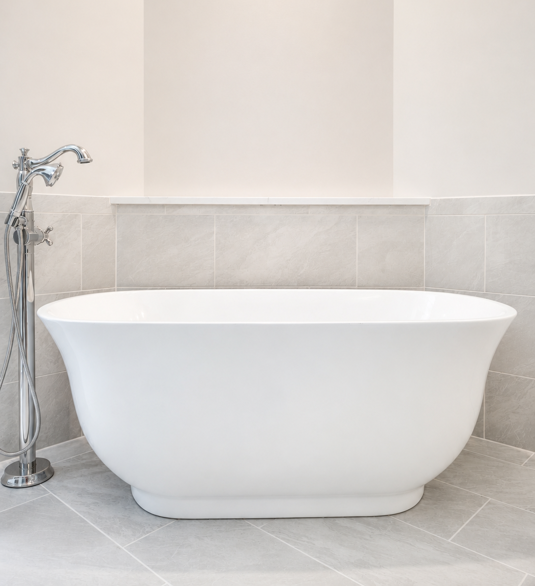 Freestanding white bathtub in a light gray tiled bathroom corner, with a chrome faucet on the left.