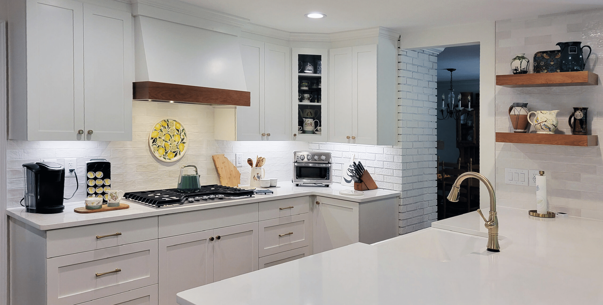 Bright modern kitchen with white cabinets, island, copper faucet, and wood shelves