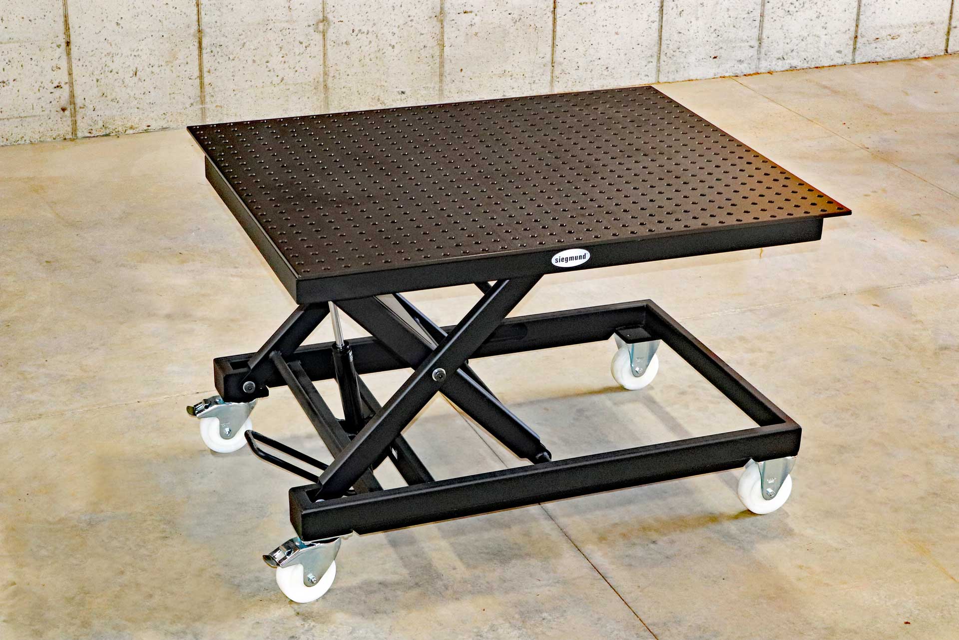 Siegmund Lifting Table A black table with white wheels is sitting on a concrete floor.