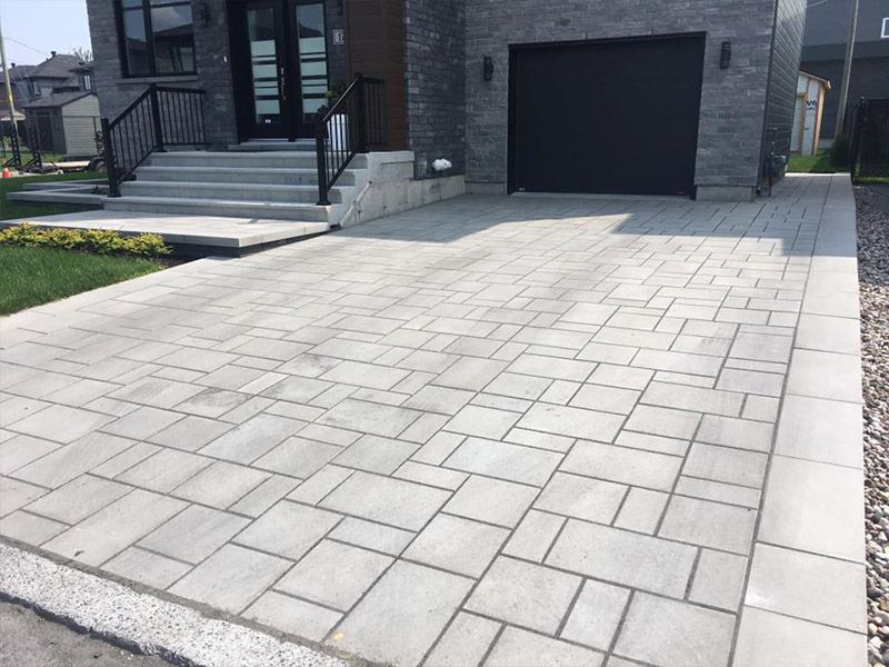 Une allée devant une maison avec une porte de garage noire.