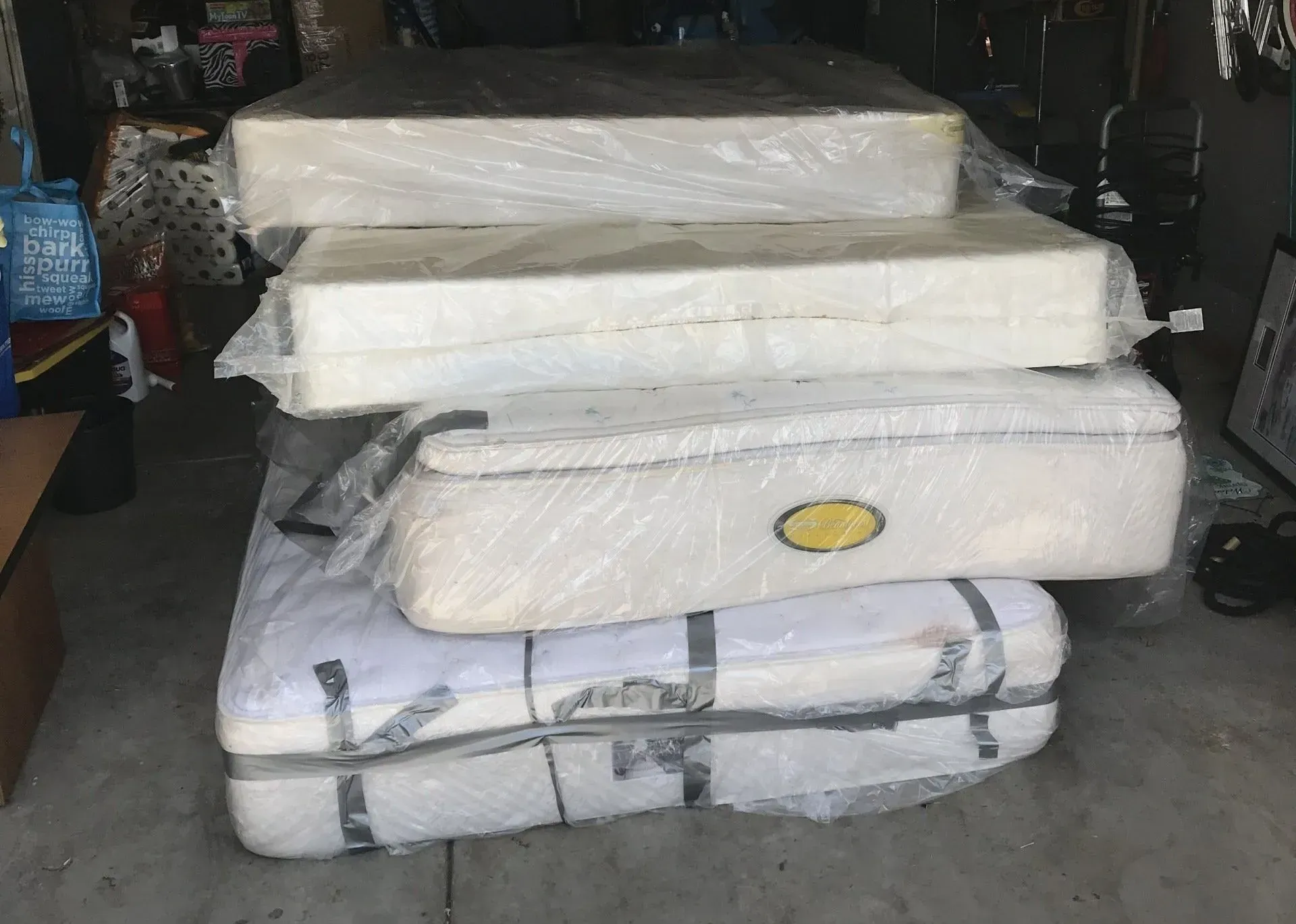 A stack of mattresses wrapped in plastic in a garage.