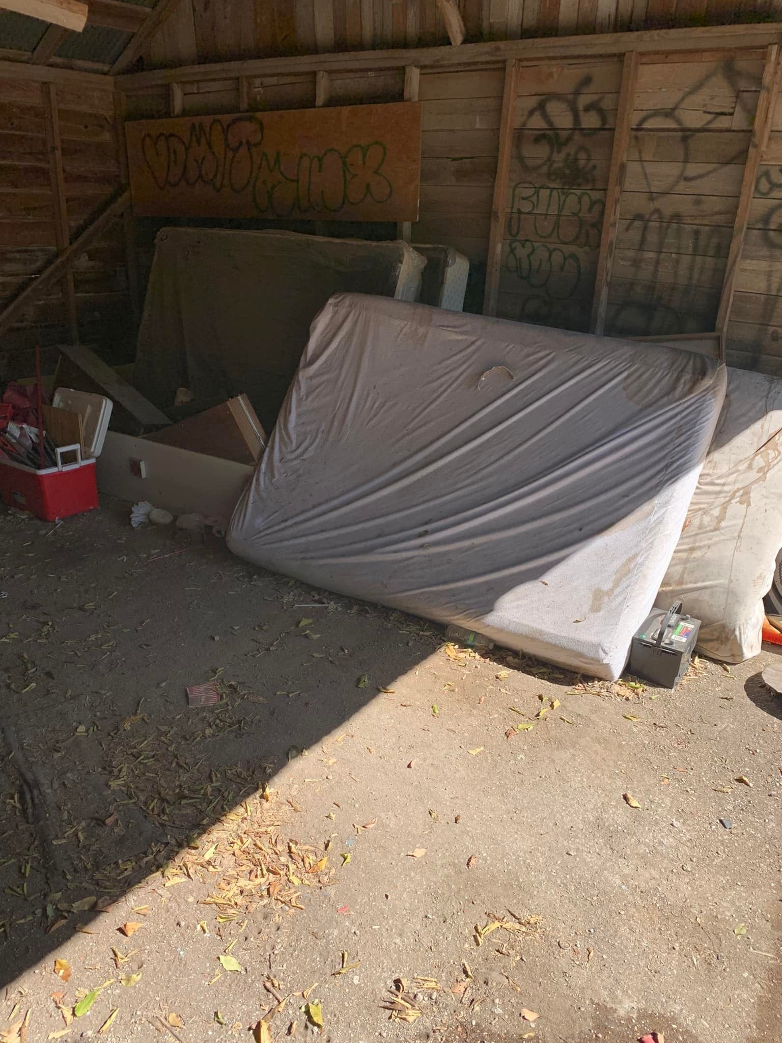 A mattress is laying on the ground in a shed.