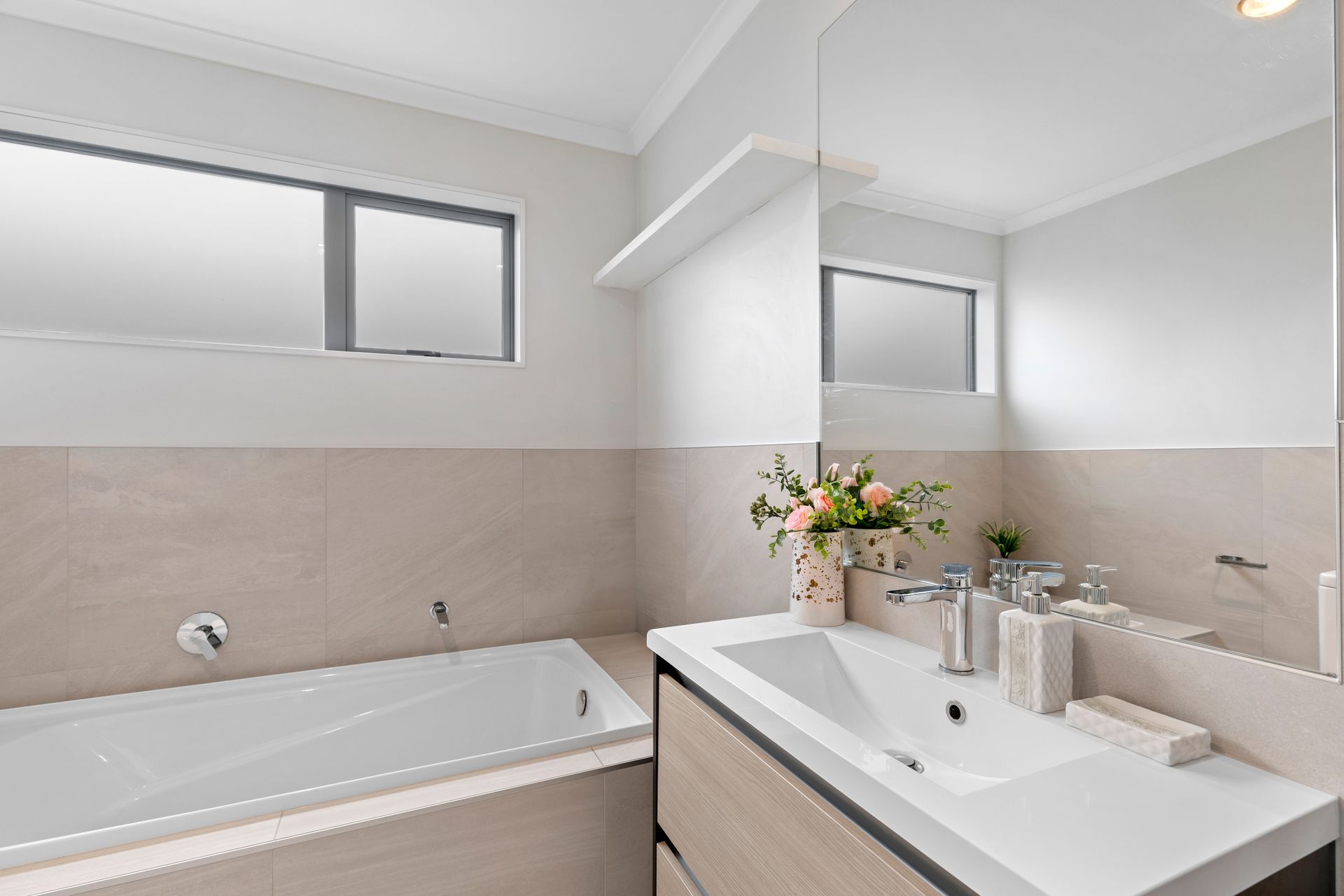 A pink tiled bathroom with a tub , sink , mirror and window.