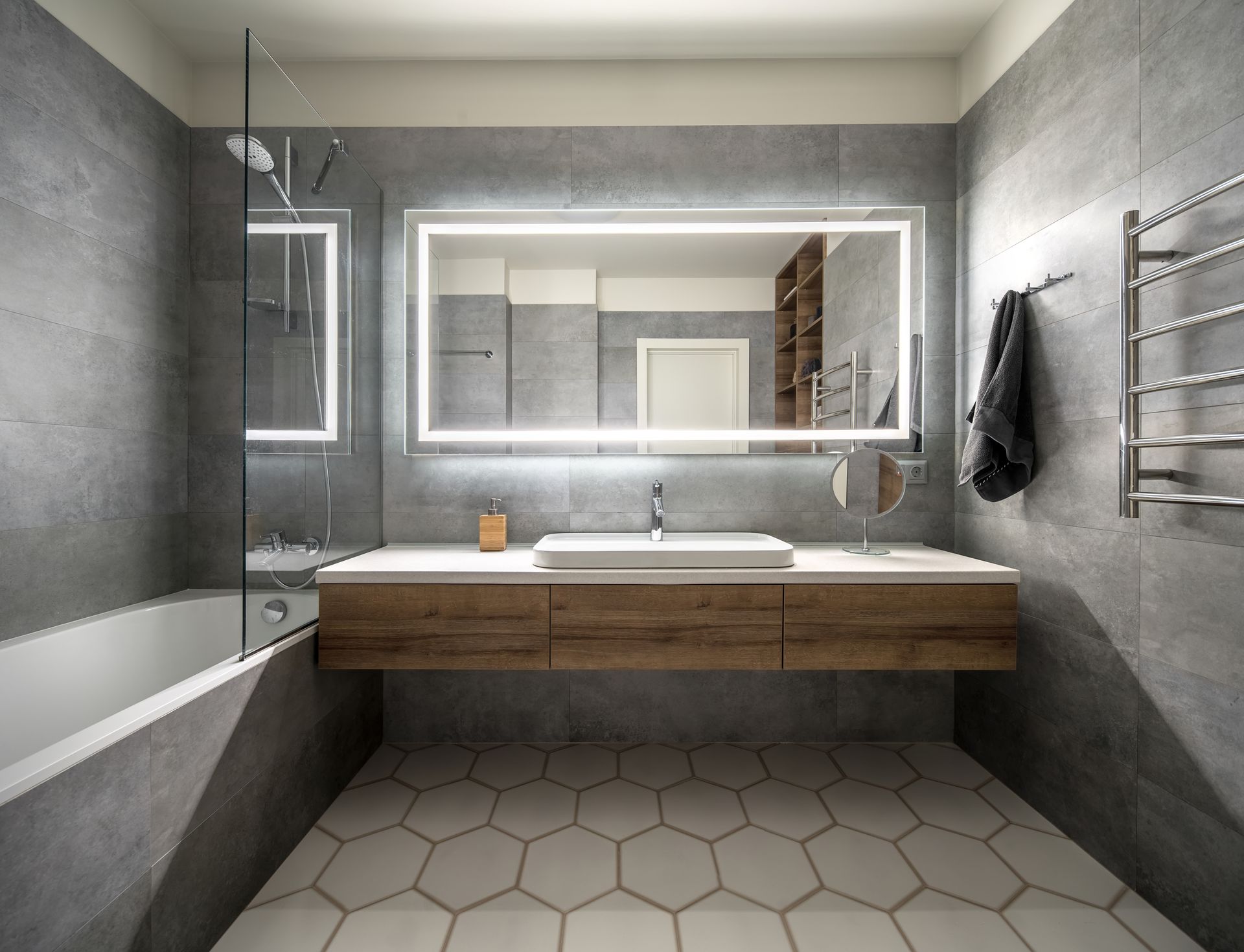 A bathroom with a sink , bathtub and LED mirror.