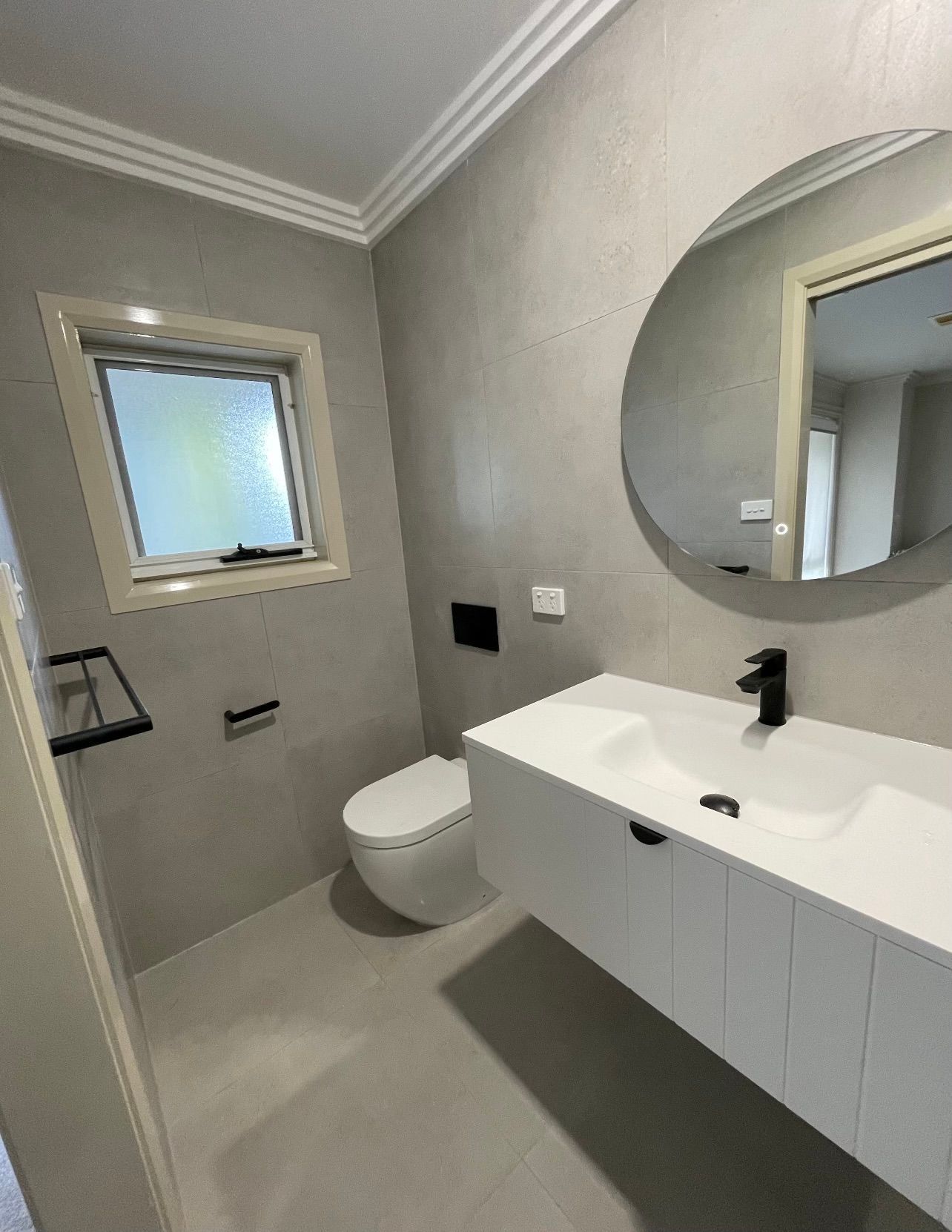 A bathroom with a toilet , sink , mirror and window.