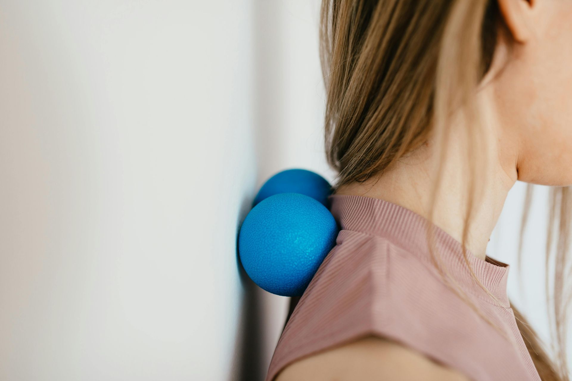 A woman is using a blue ball to massage her neck.