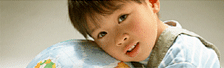 A young child resting their head on a globe, looking towards the viewer with a thoughtful expression.