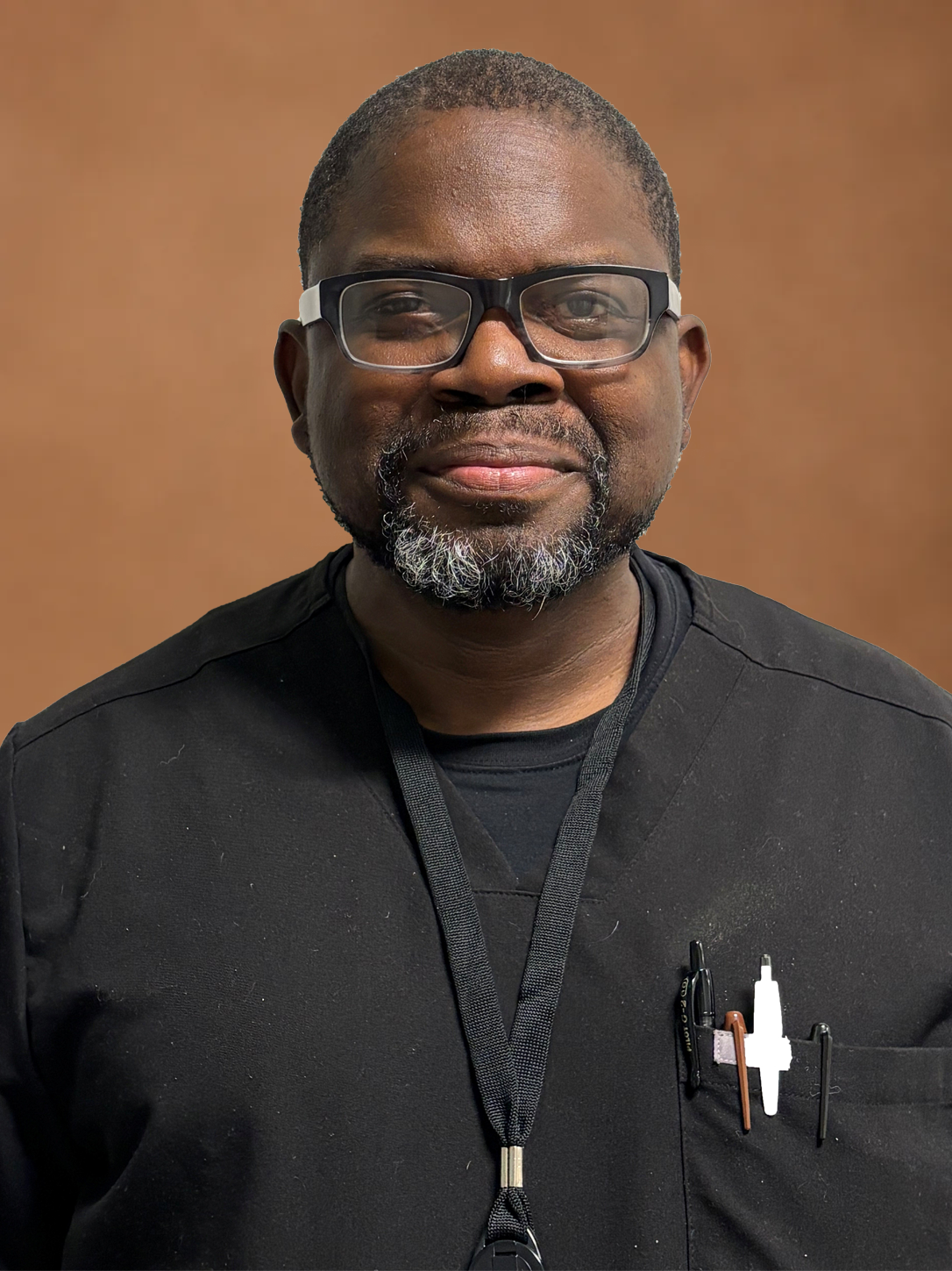 Portrait of a man in glasses and a black shirt, smiling against a brown background