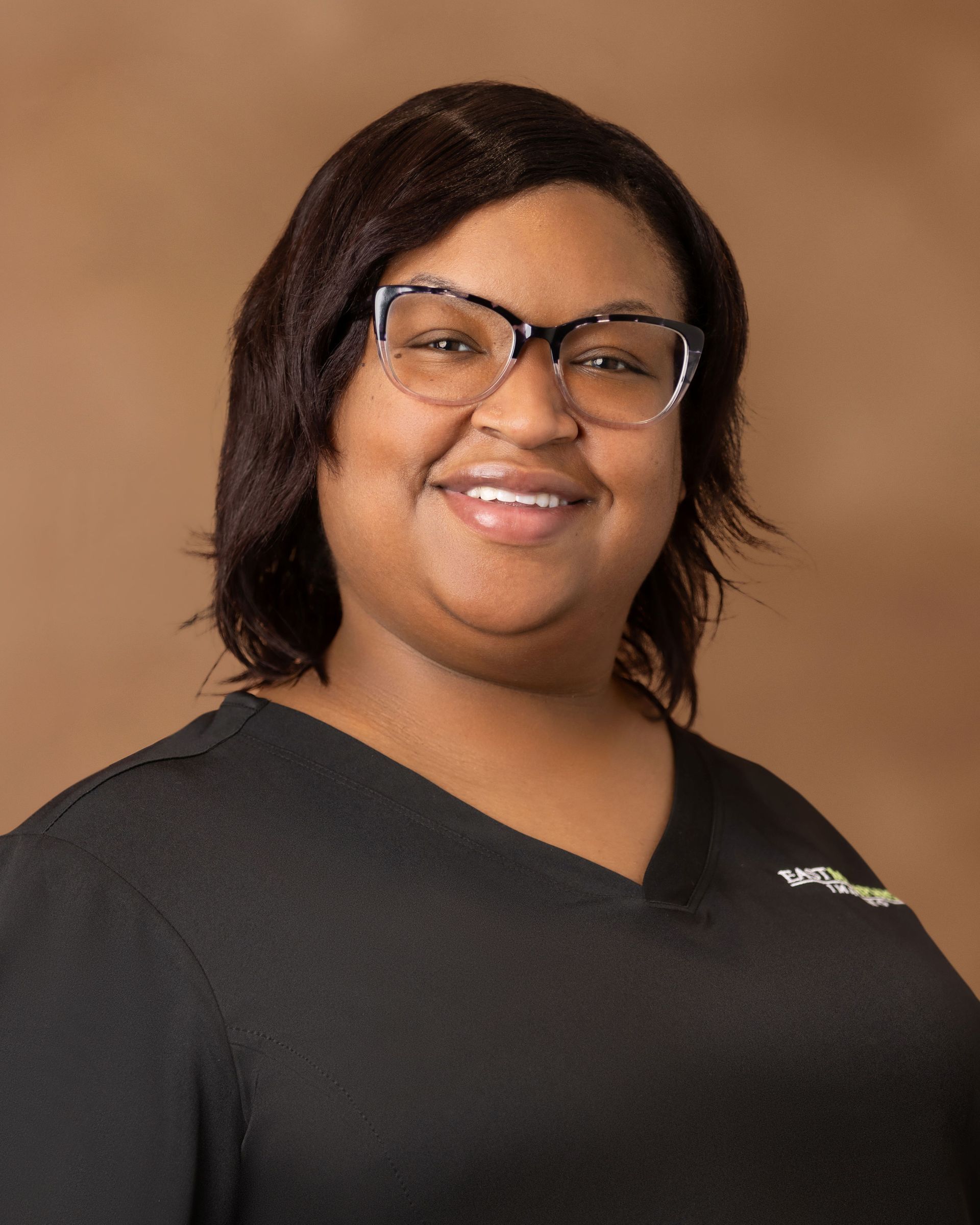 Smiling person in glasses wearing a black shirt against a warm brown background