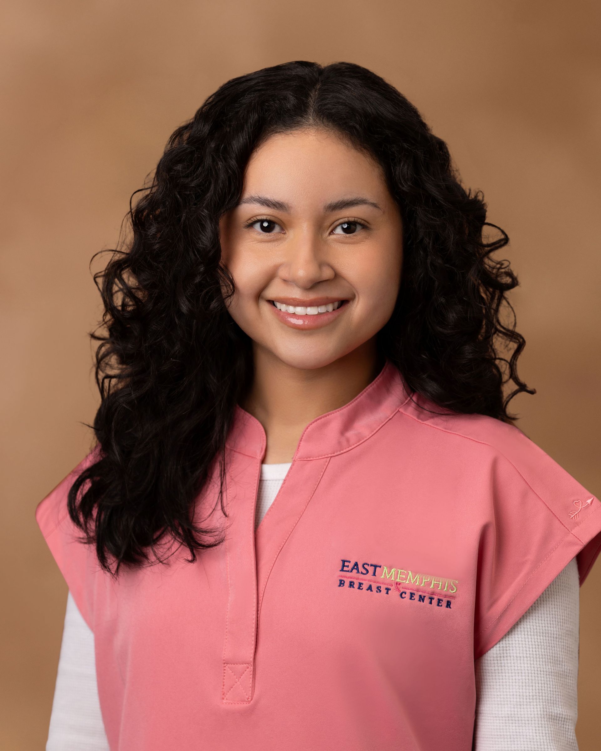 Smiling person in a pink vest against a tan background.