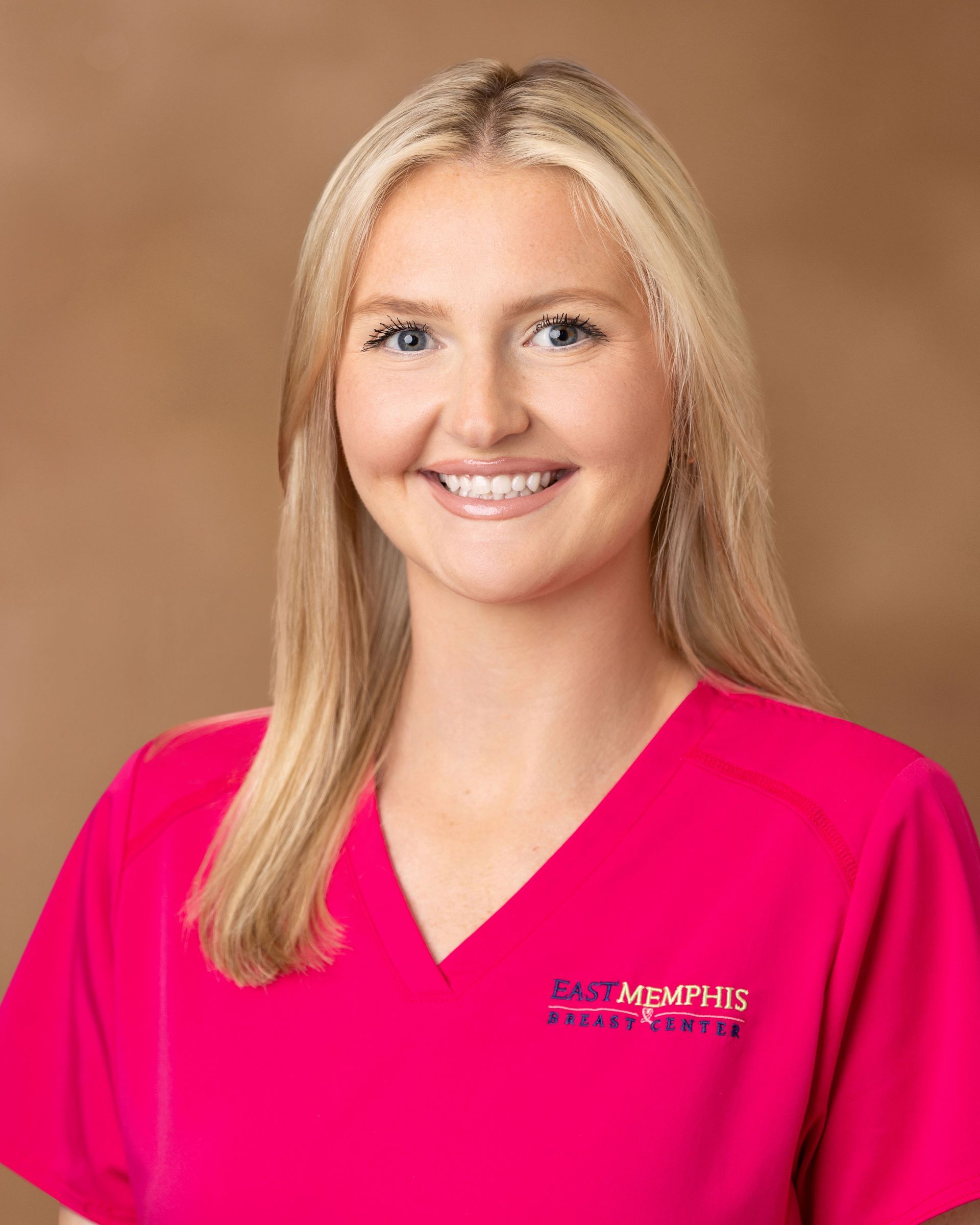 Smiling woman in bright pink uniform against a tan studio backdrop