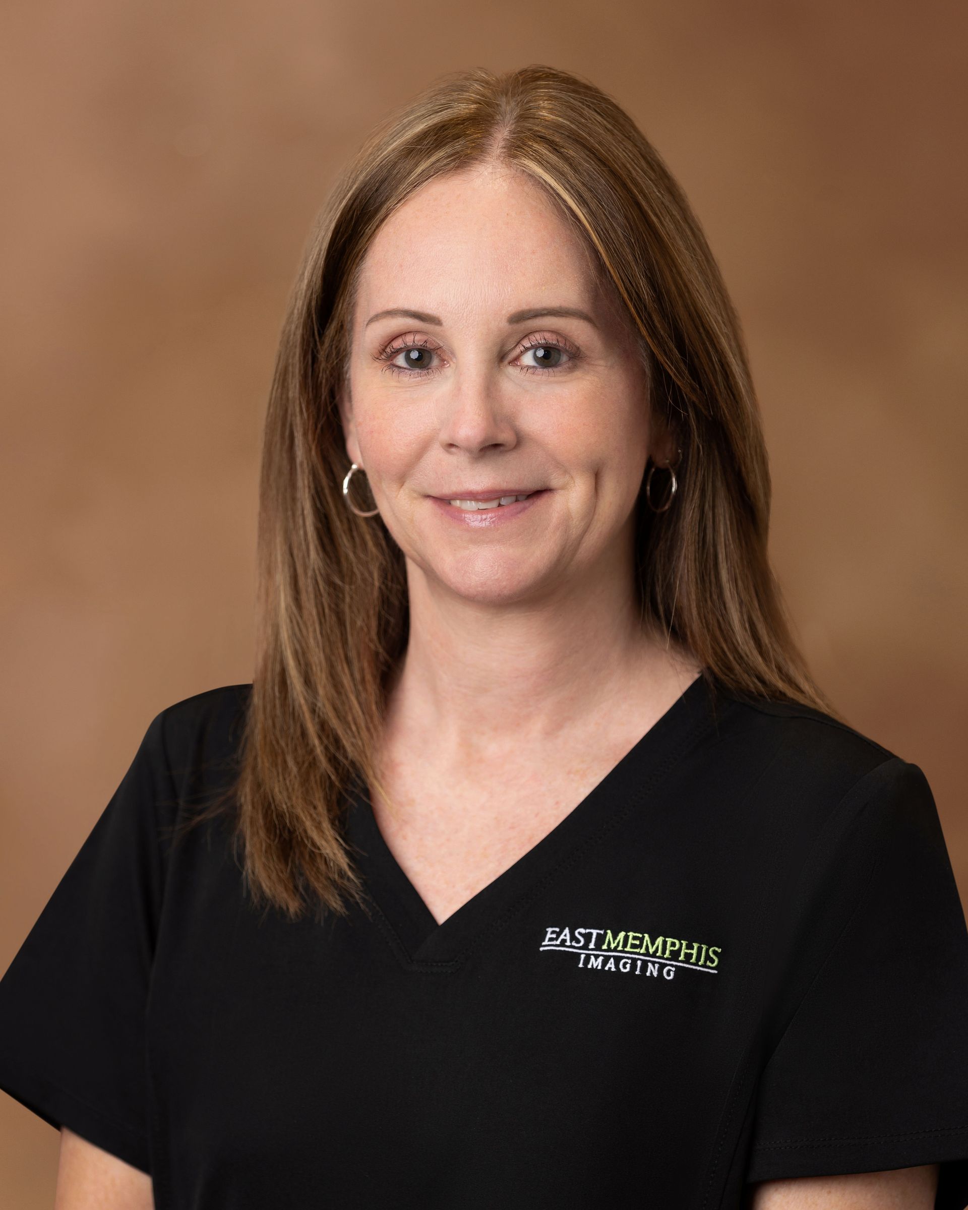 Portrait of a woman in a black V-neck top against a brown studio backdrop