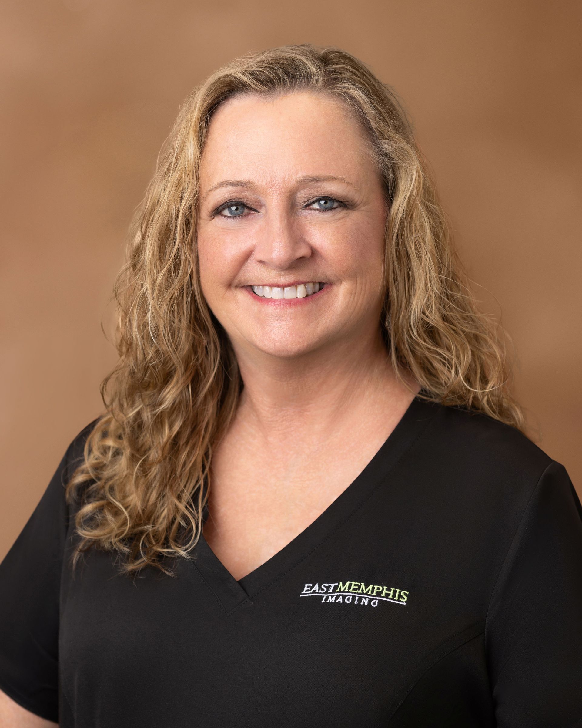 Smiling woman in a black V-neck top against a tan studio background