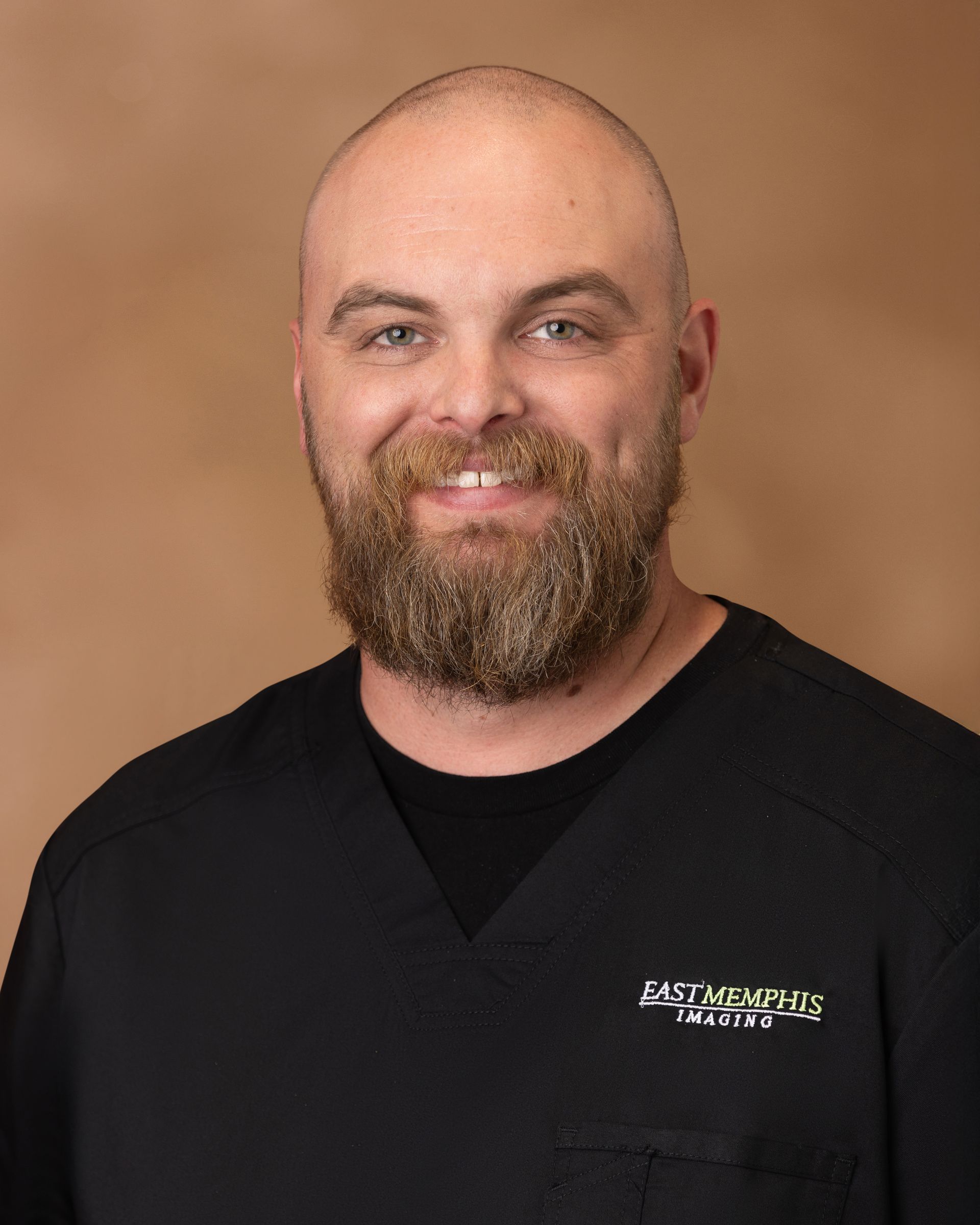 Portrait of a smiling bald man with a beard wearing a black shirt against a tan background