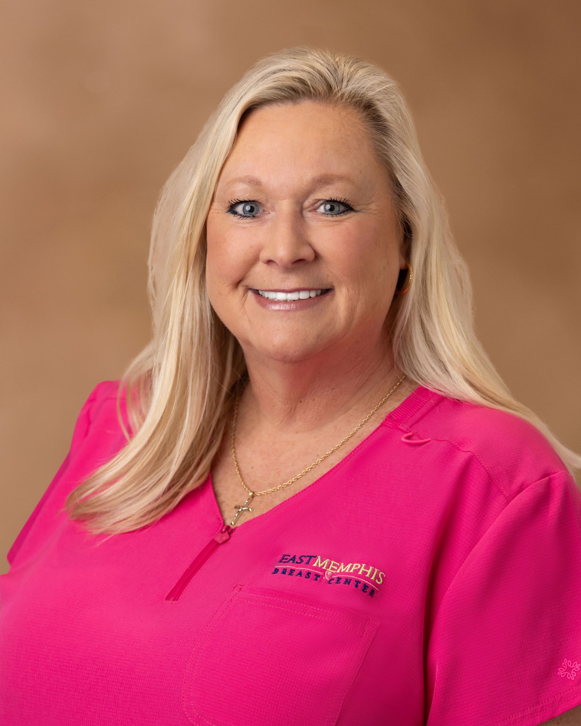 Portrait of a smiling blonde woman in a bright pink blouse against a tan background