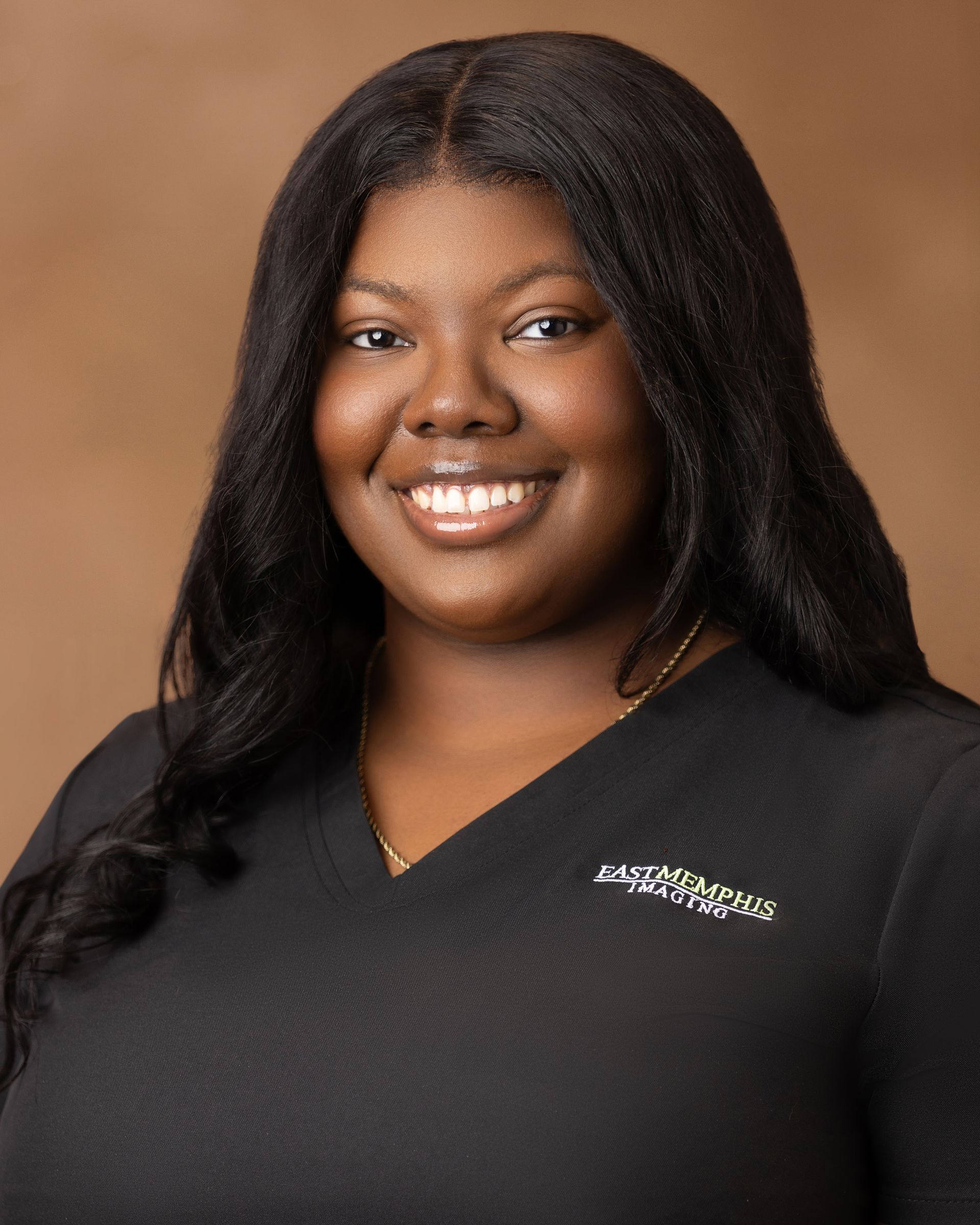 Smiling person in a black top against a warm brown studio background.