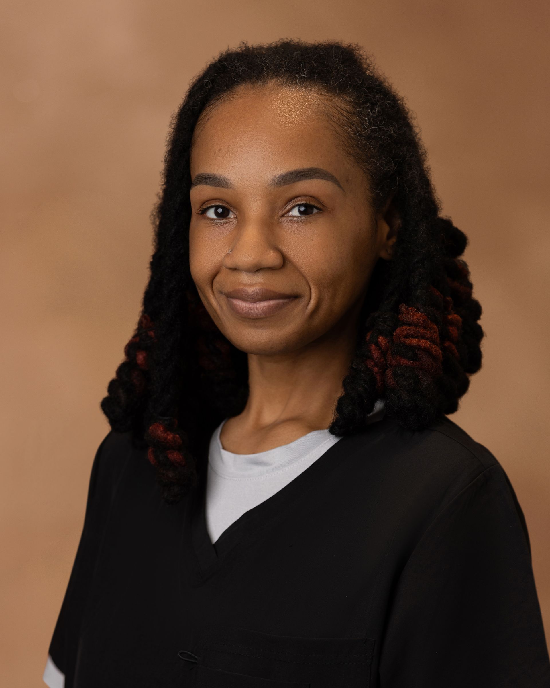 Portrait of a smiling person in a black top against a warm brown studio backdrop