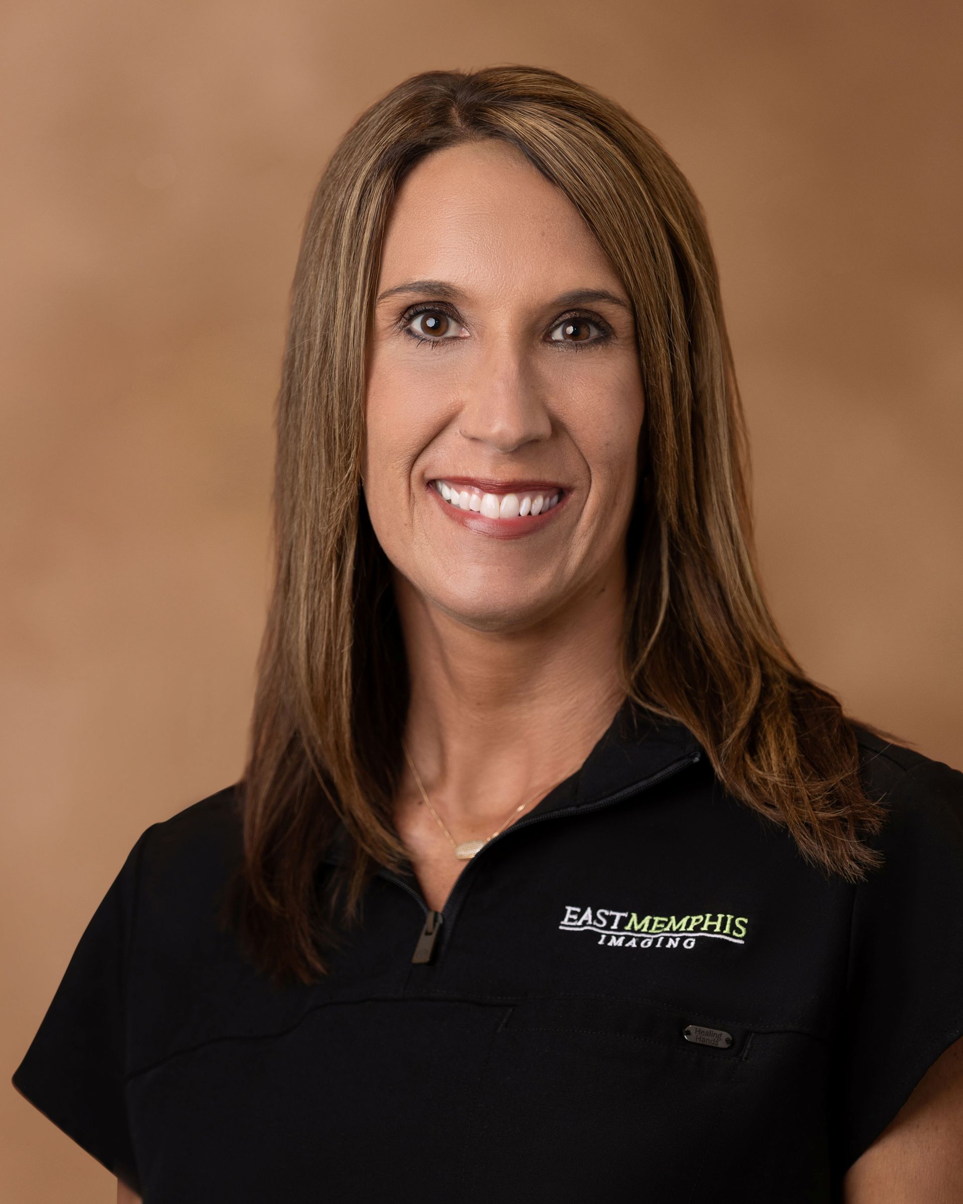 Woman in black collared shirt smiling against a tan studio backdrop