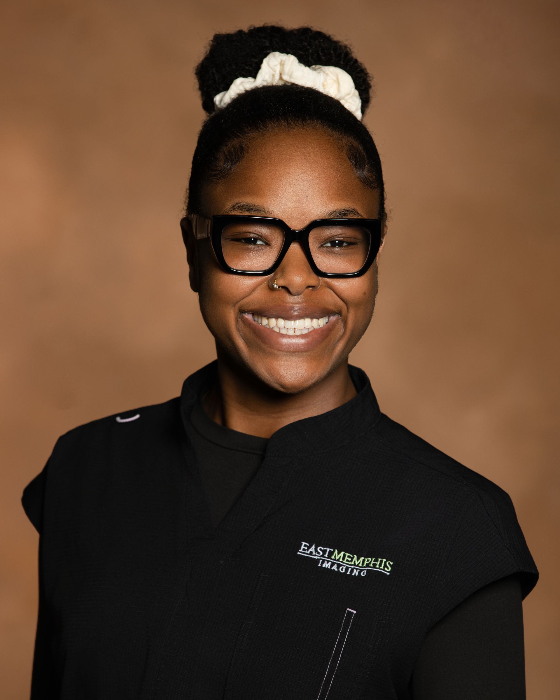 Smiling person in black shirt and glasses against a brown background.