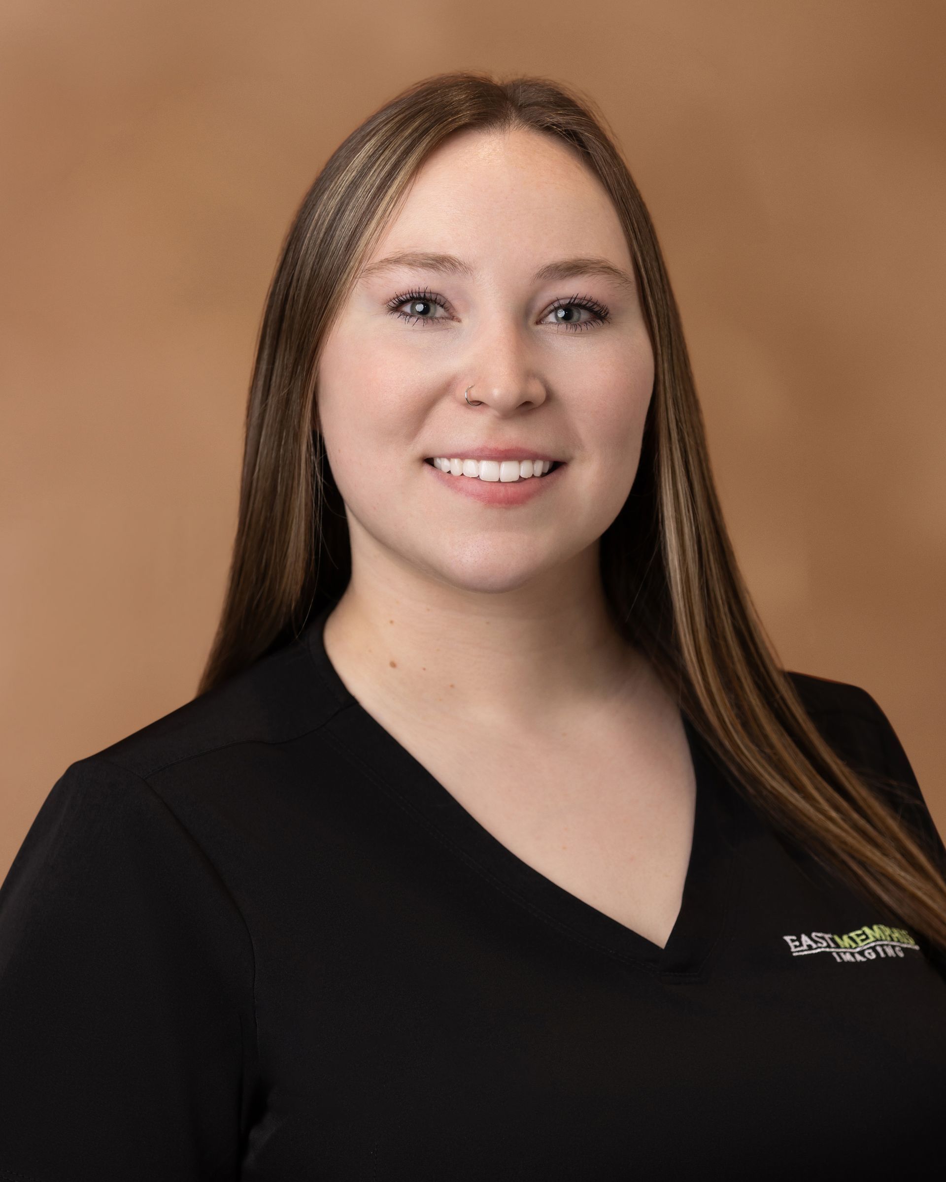Portrait of a smiling woman in a black V-neck top against a tan studio background