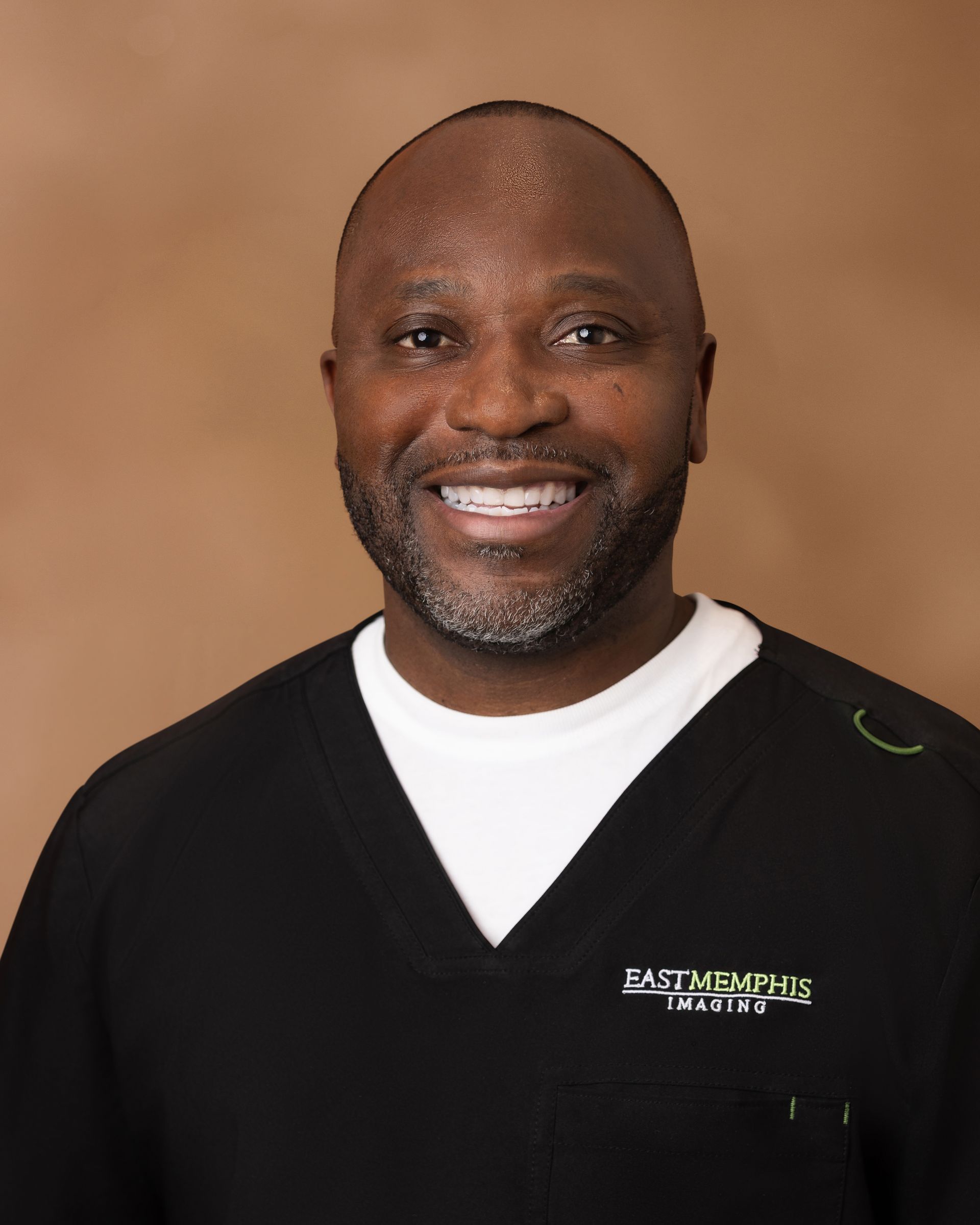 Smiling person in a black V-neck sweater over a white shirt against a tan background