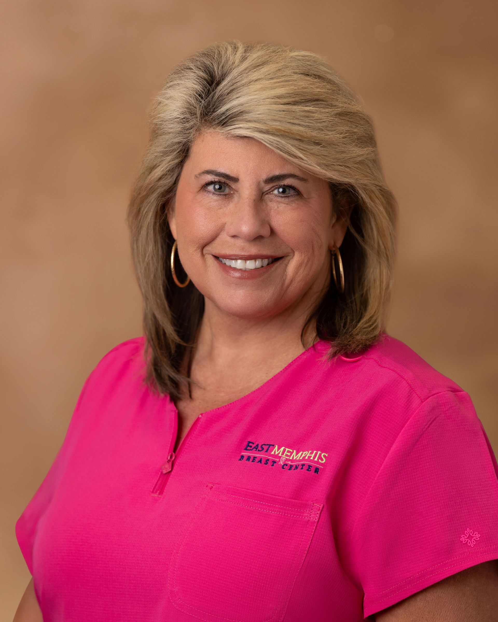 Smiling woman in a bright pink top against a tan studio backdrop