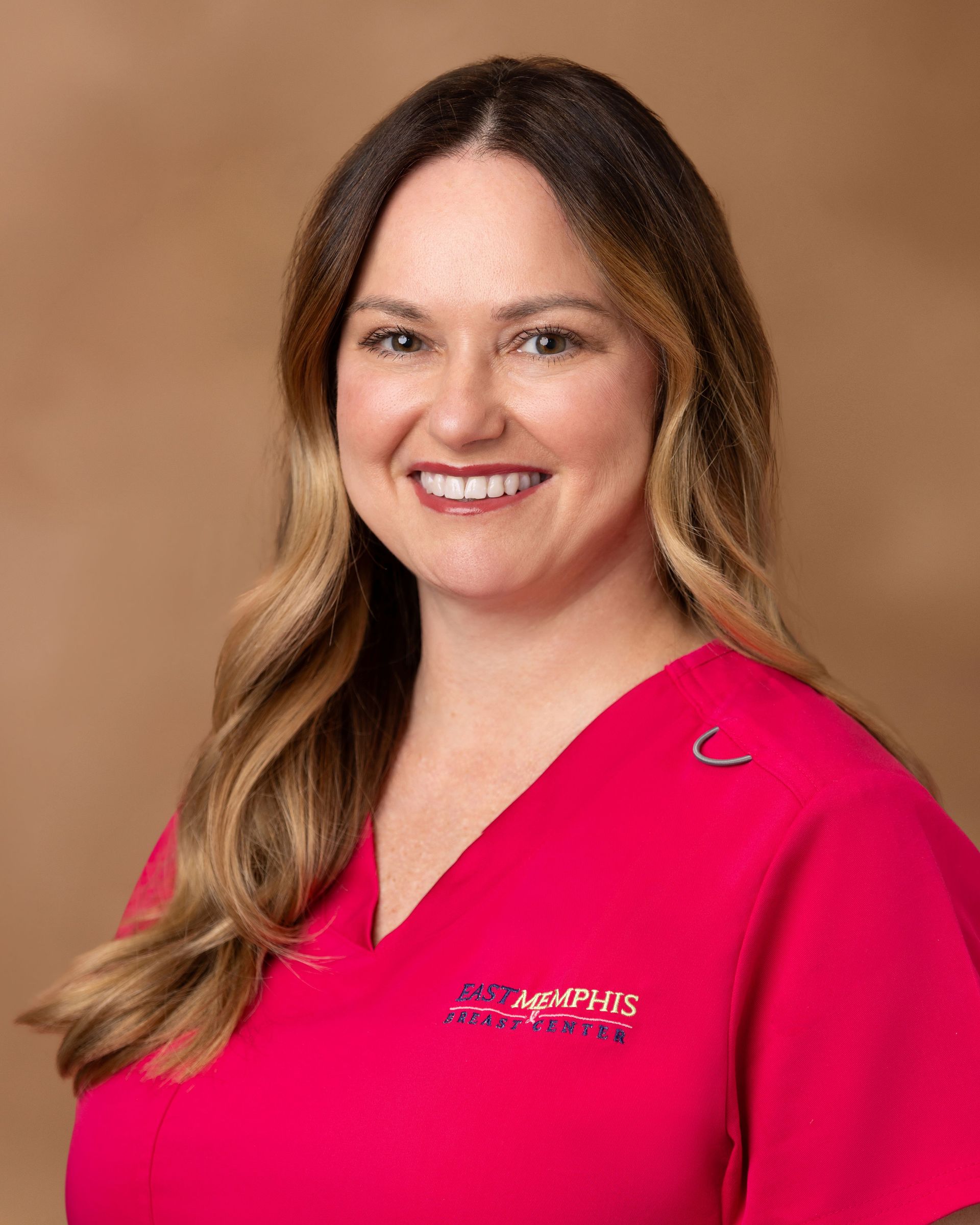 Woman smiling in a bright pink top against a tan studio backdrop