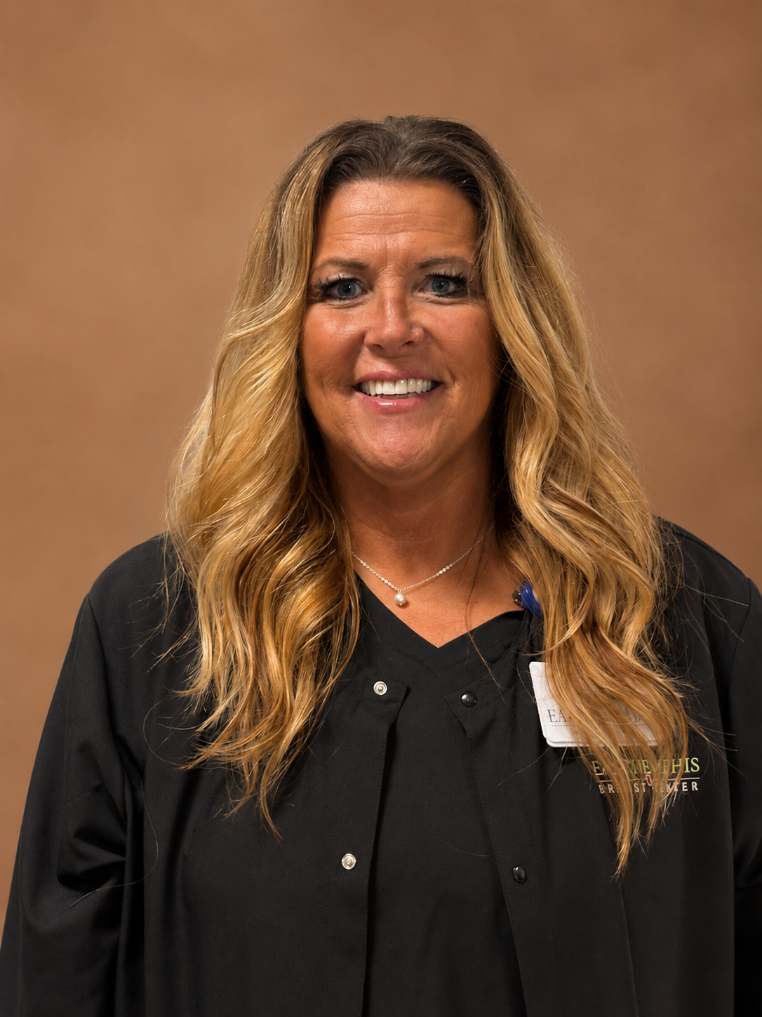Smiling woman in black top and cardigan against a brown backdrop.