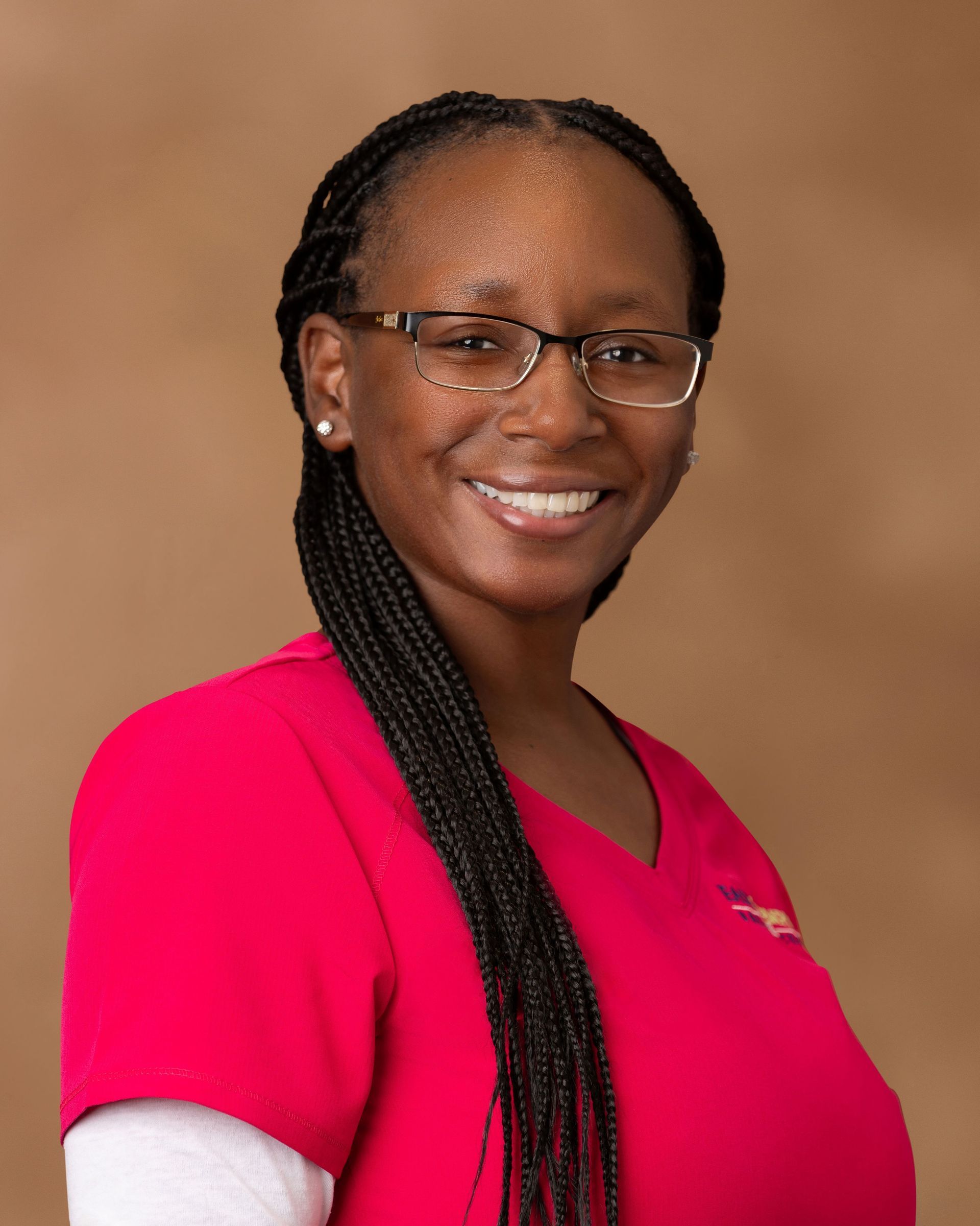 Smiling person in a bright pink top with glasses against a tan studio backdrop