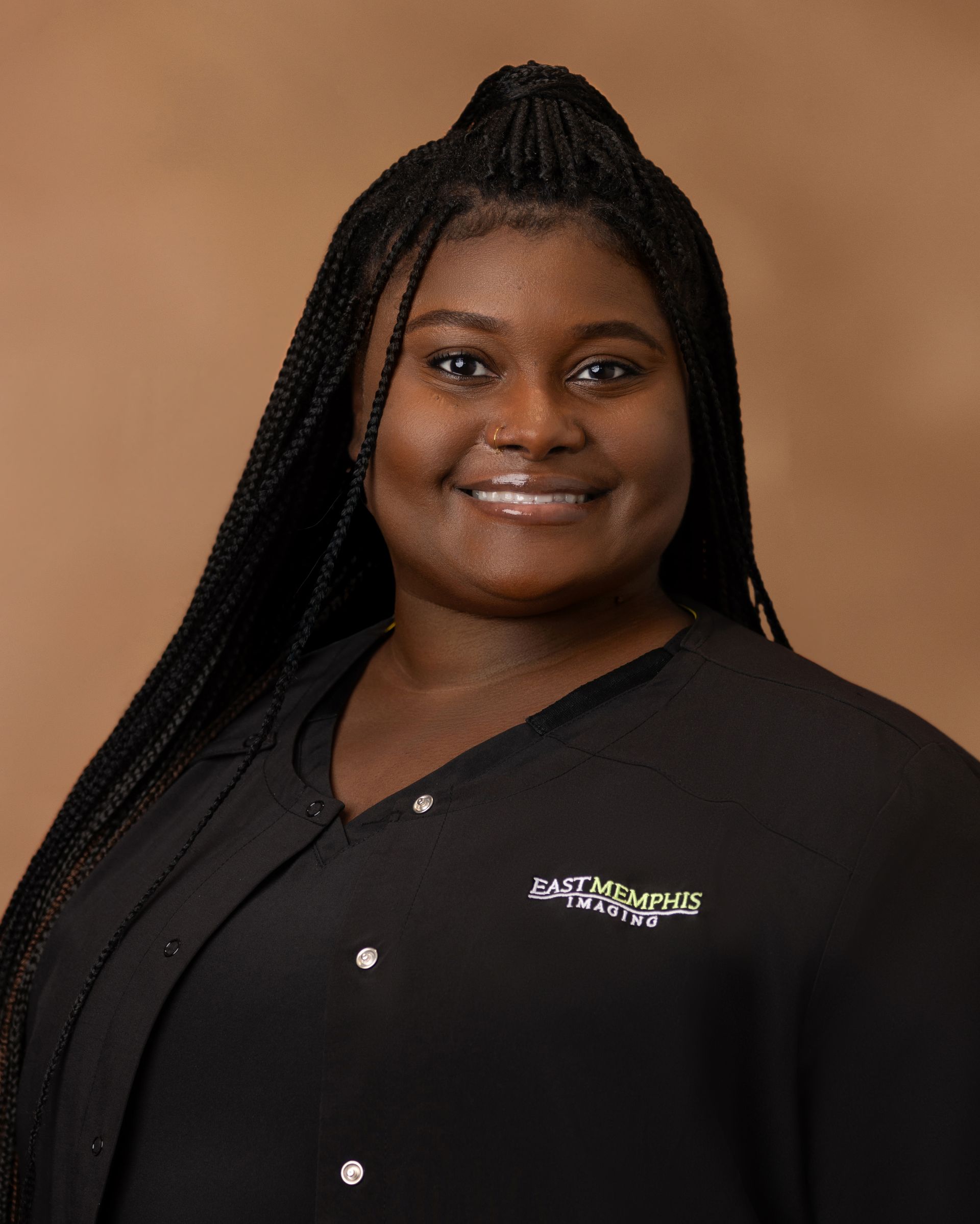 Smiling person in a black collared shirt against a tan background