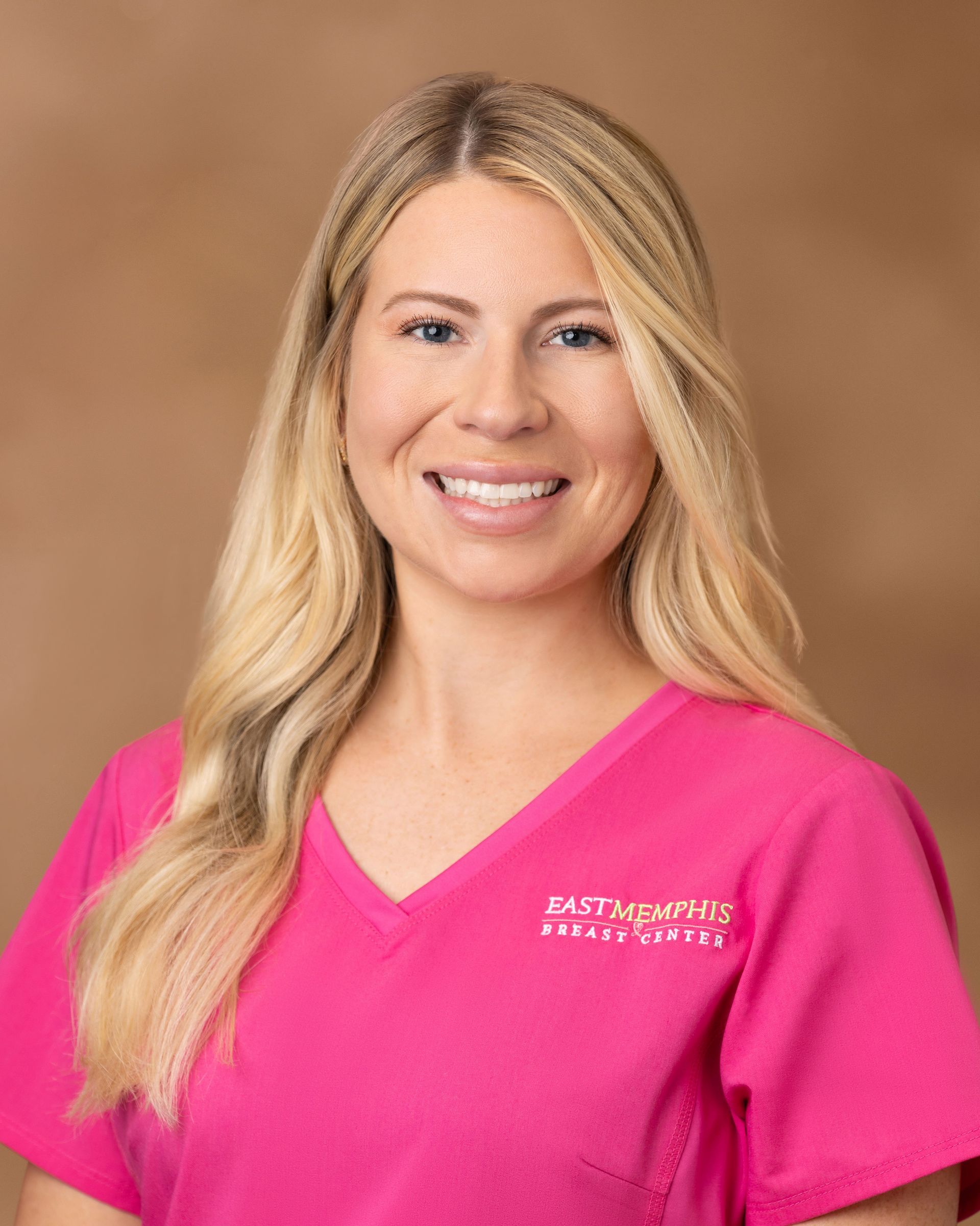 Smiling blonde woman in a bright pink top against a tan studio background