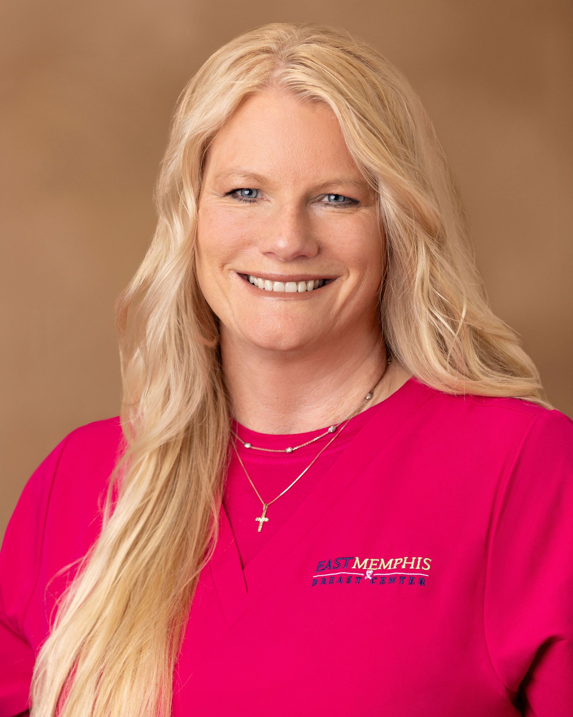 Smiling woman in a bright pink shirt against a warm tan background.