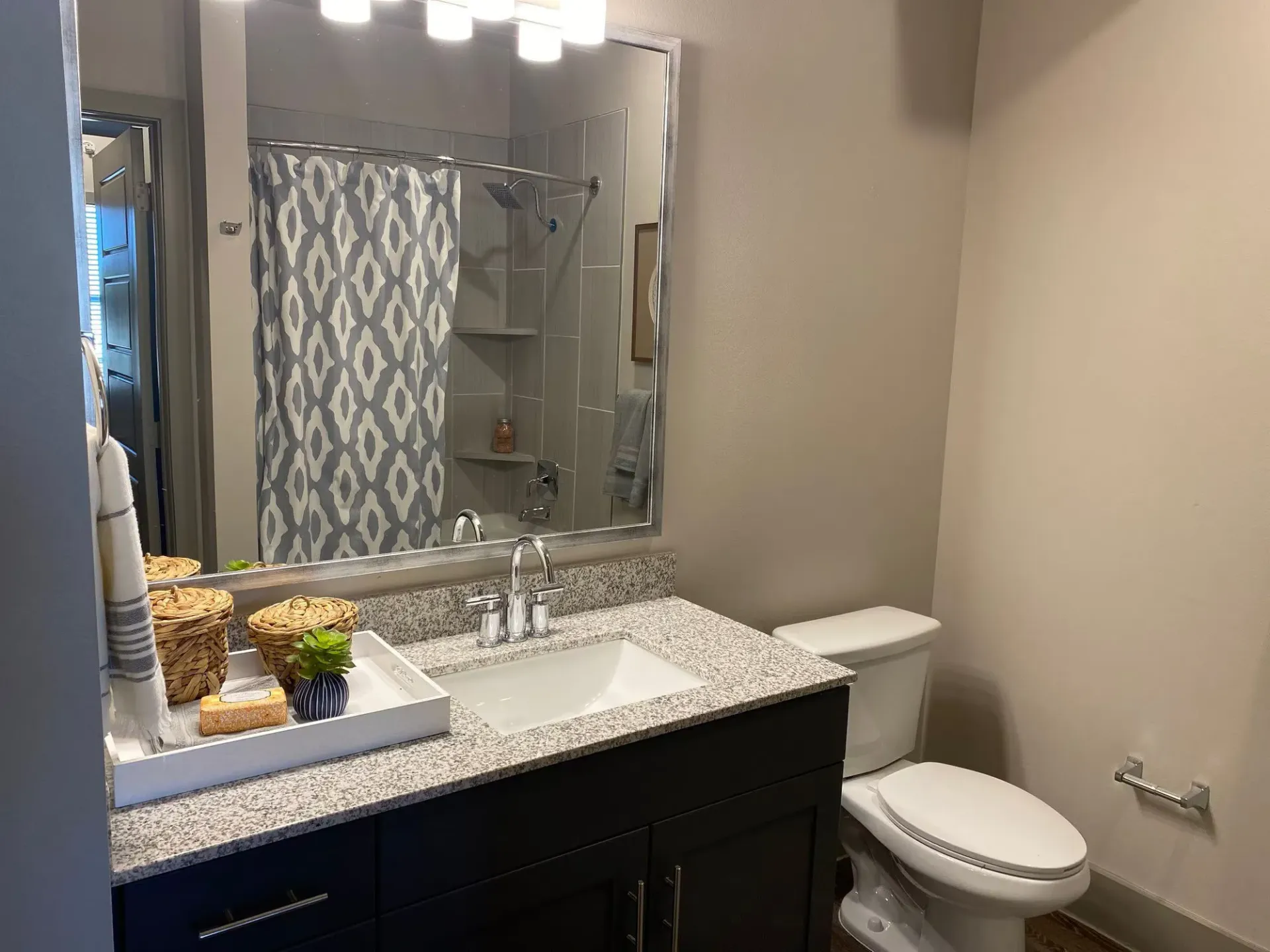 Bathroom with granite vanity, large mirror, toilet, and shower with a blue patterned curtain.