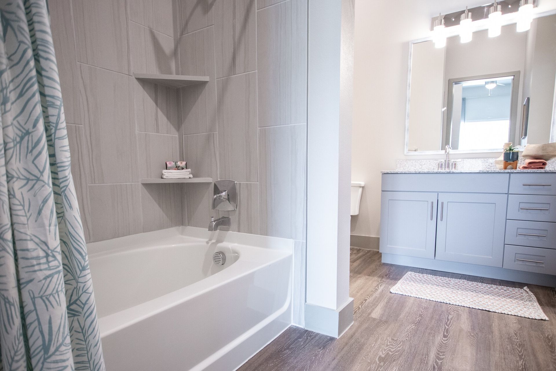 Apartment bathroom with tub/shower, vanity, mirror, and built-in shelves.