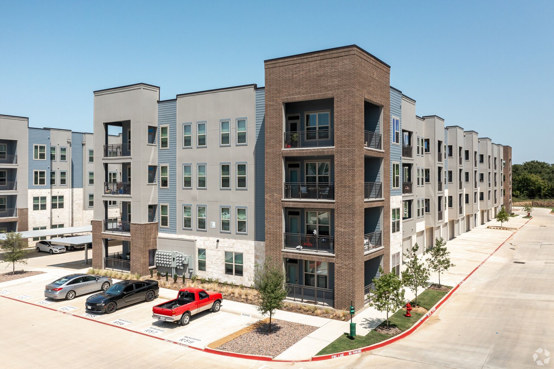 Exterior view of a modern apartment building with balconies and a parking lot.