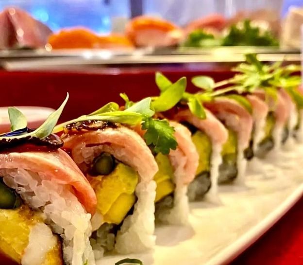 Sushi rolls topped with salmon and herbs on a white platter, lined up at a buffet.