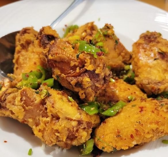 Plate of golden fried chicken pieces topped with chopped green peppers and spices