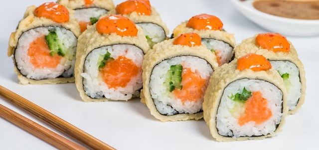 Sushi rolls topped with orange roe, served on chopsticks against a white background
