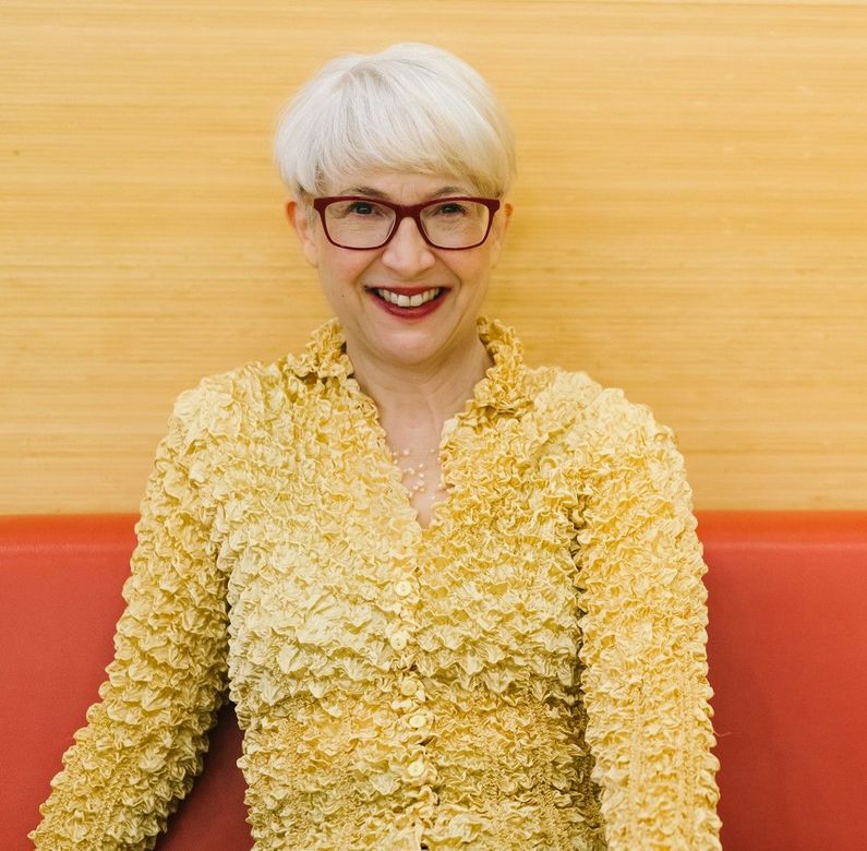 Andrea wears glasses and a pink top and is leaning on a railing.
