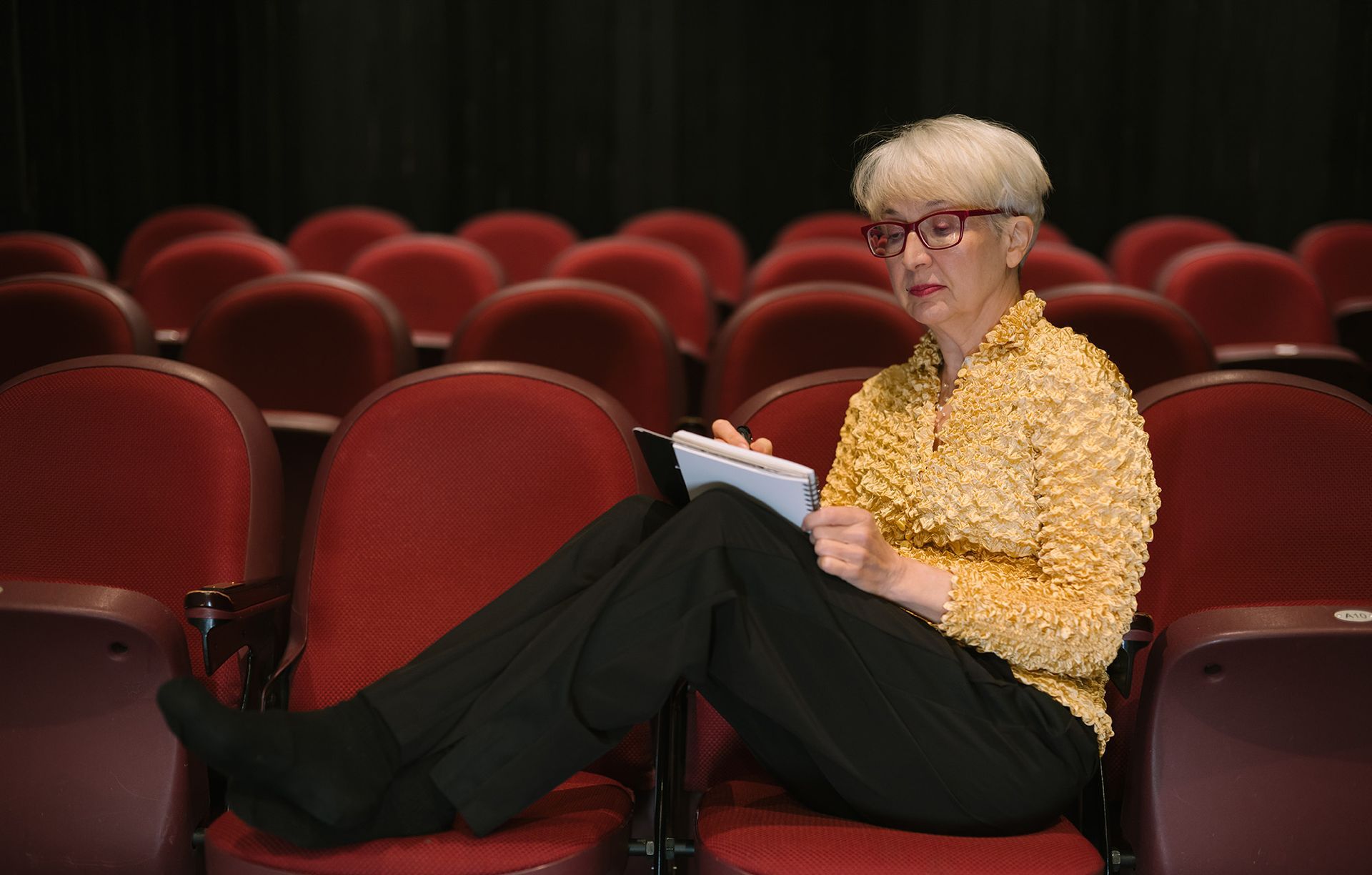 Andrea is sitting in an auditorium with her legs crossed and writing on a pad of paper.