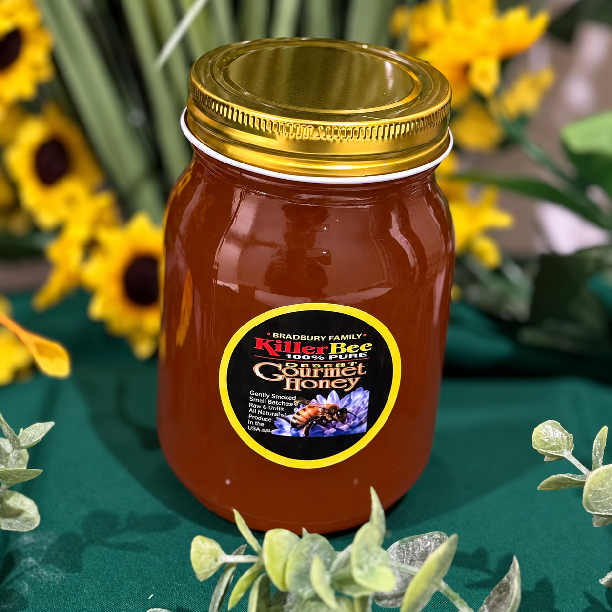 Jar of amber honey with gold lid and label, set among yellow flowers on a green cloth